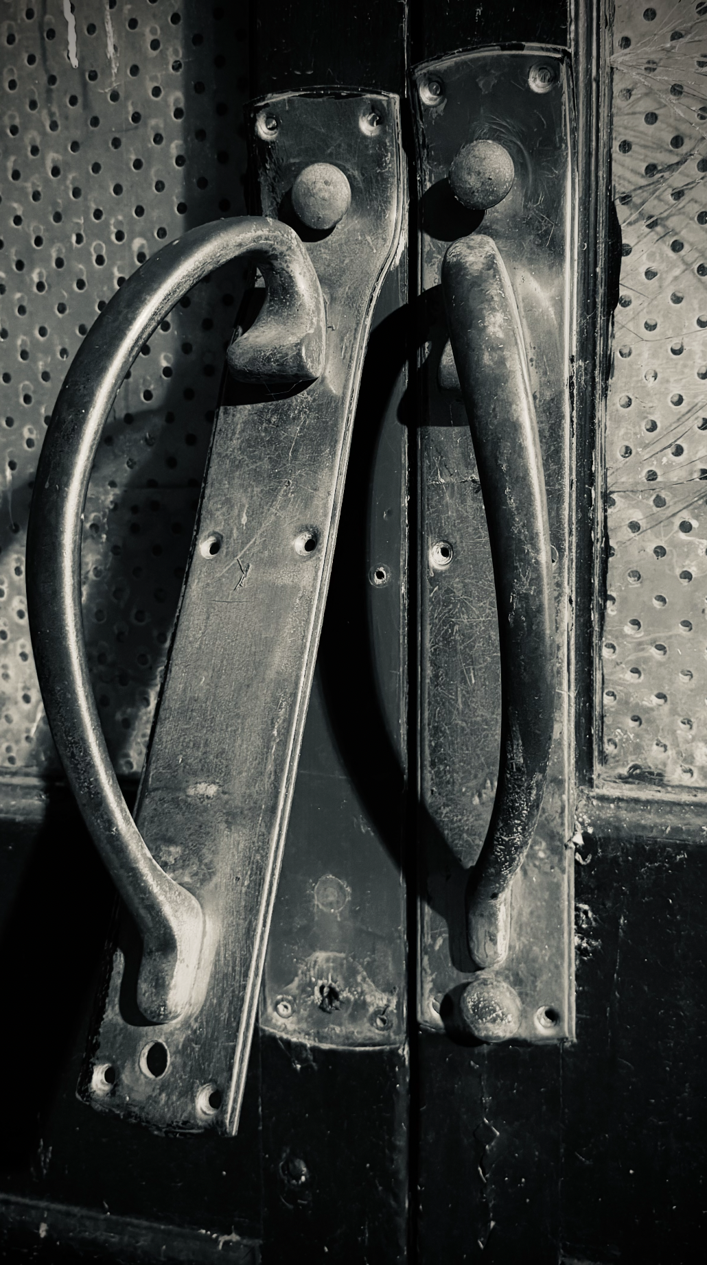 Close-up of a black metal door with two old, dusty, metal handles.