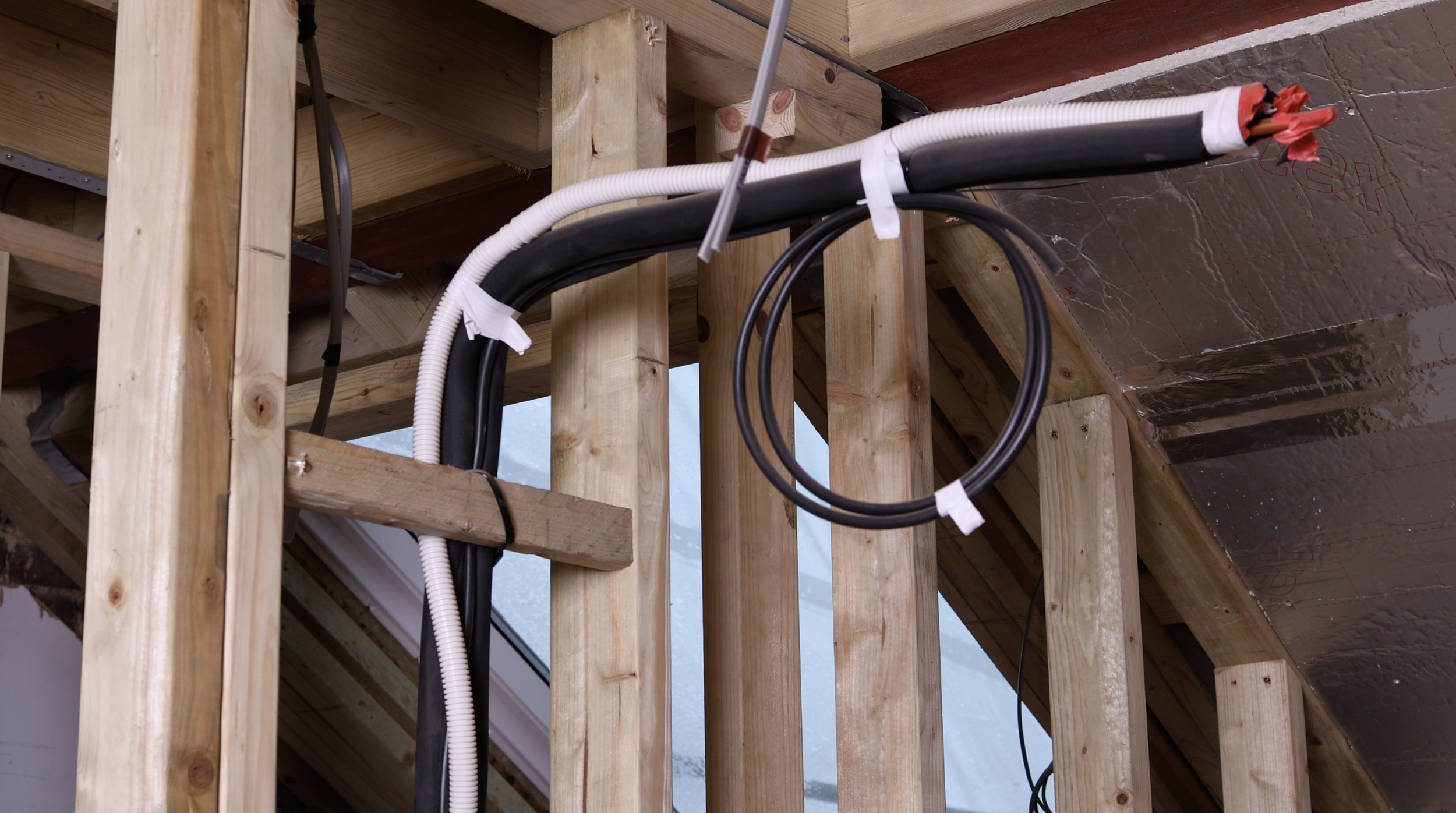 Electrical cables and conduit installed through wooden framing of a building under construction, with ceiling insulation visible.
