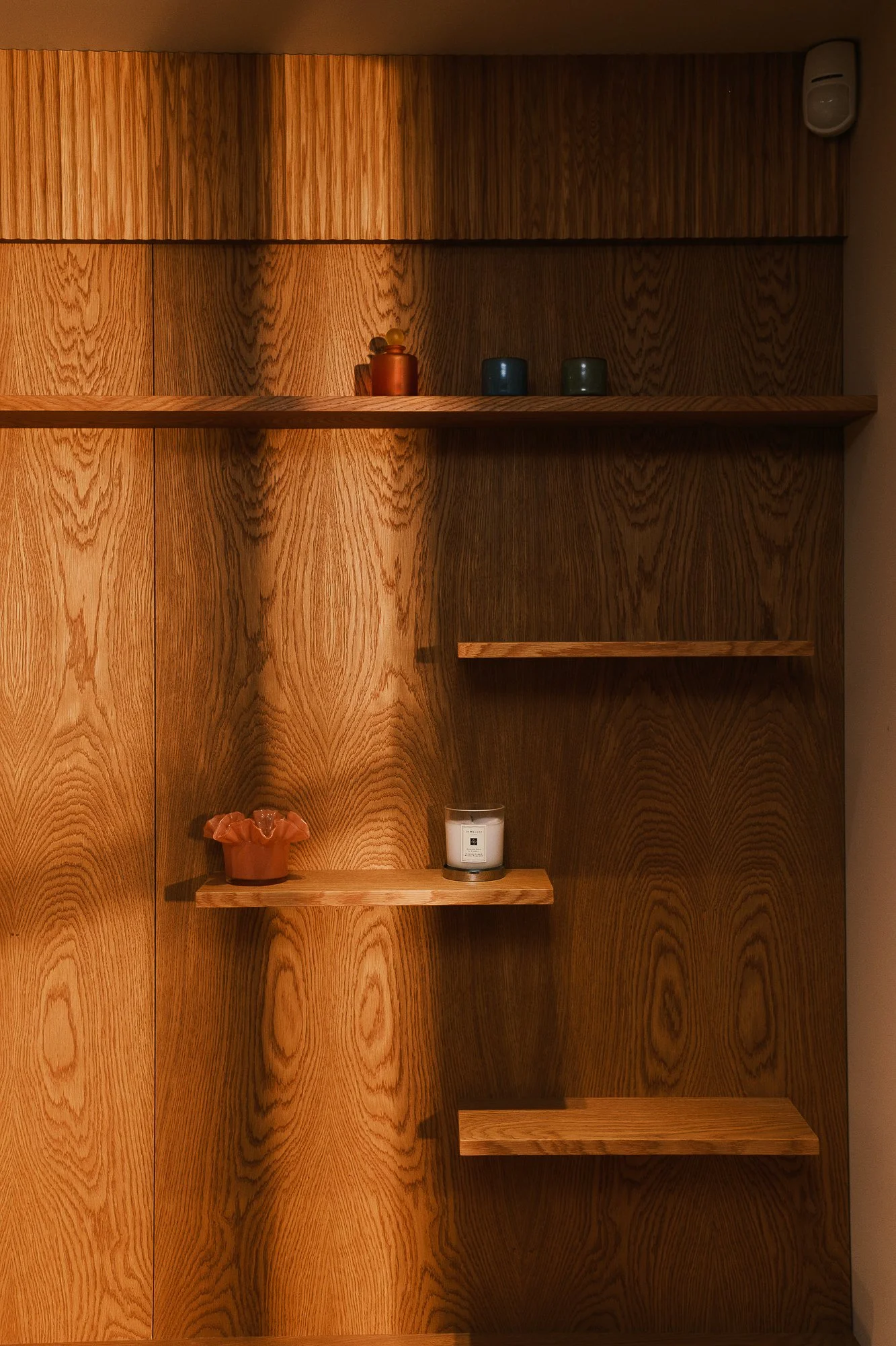 Wooden wall with several shelves holding small decorative items and a candle.