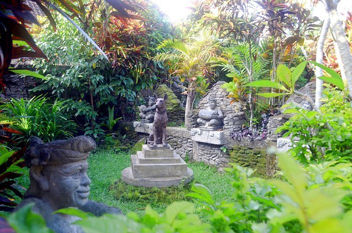 Lush tropical garden with stone statues, including an animal on a pedestal, surrounded by dense greenery and vibrant plants.