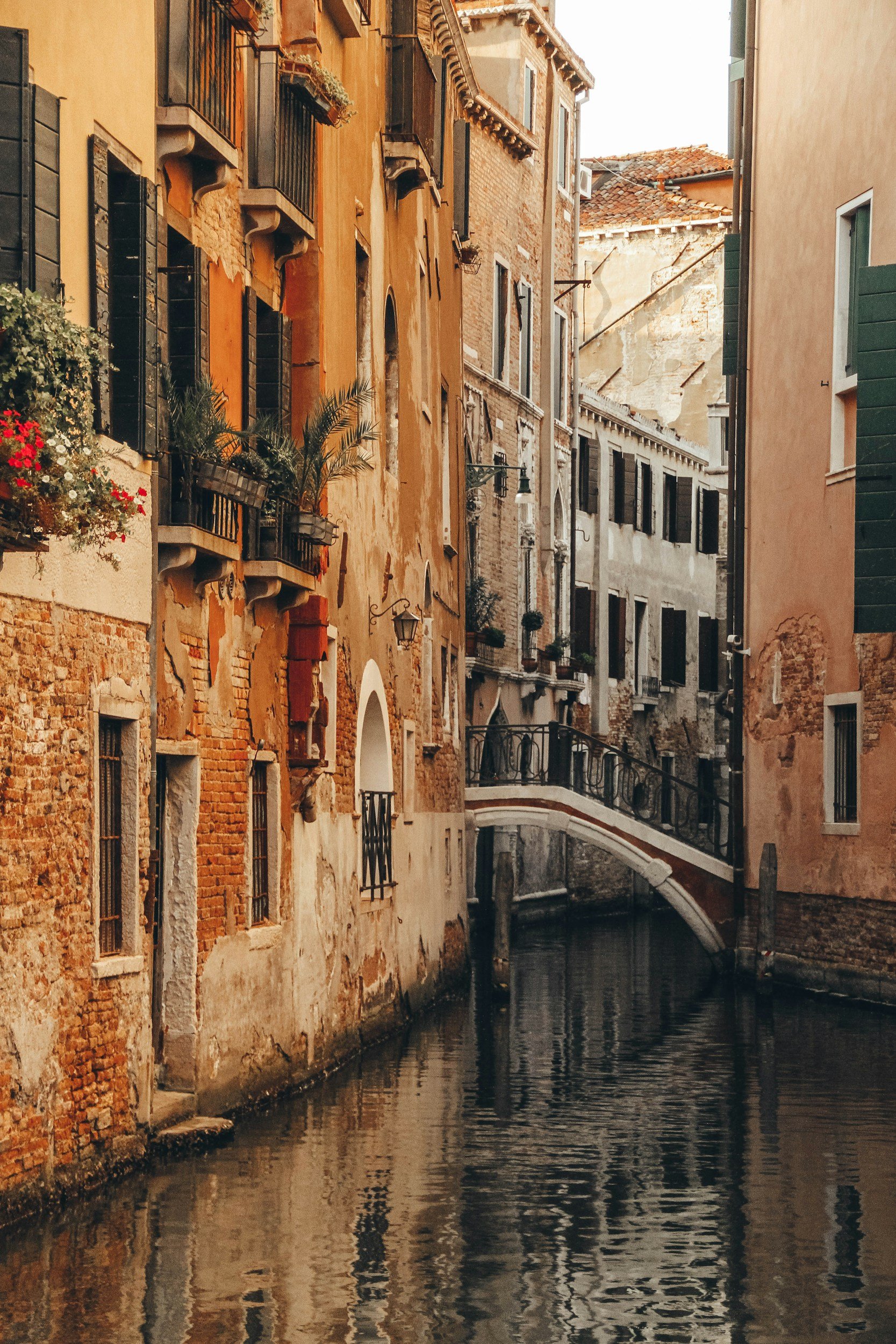 Narrow canal in Venice with rustic buildings and a small arched bridge in the background.