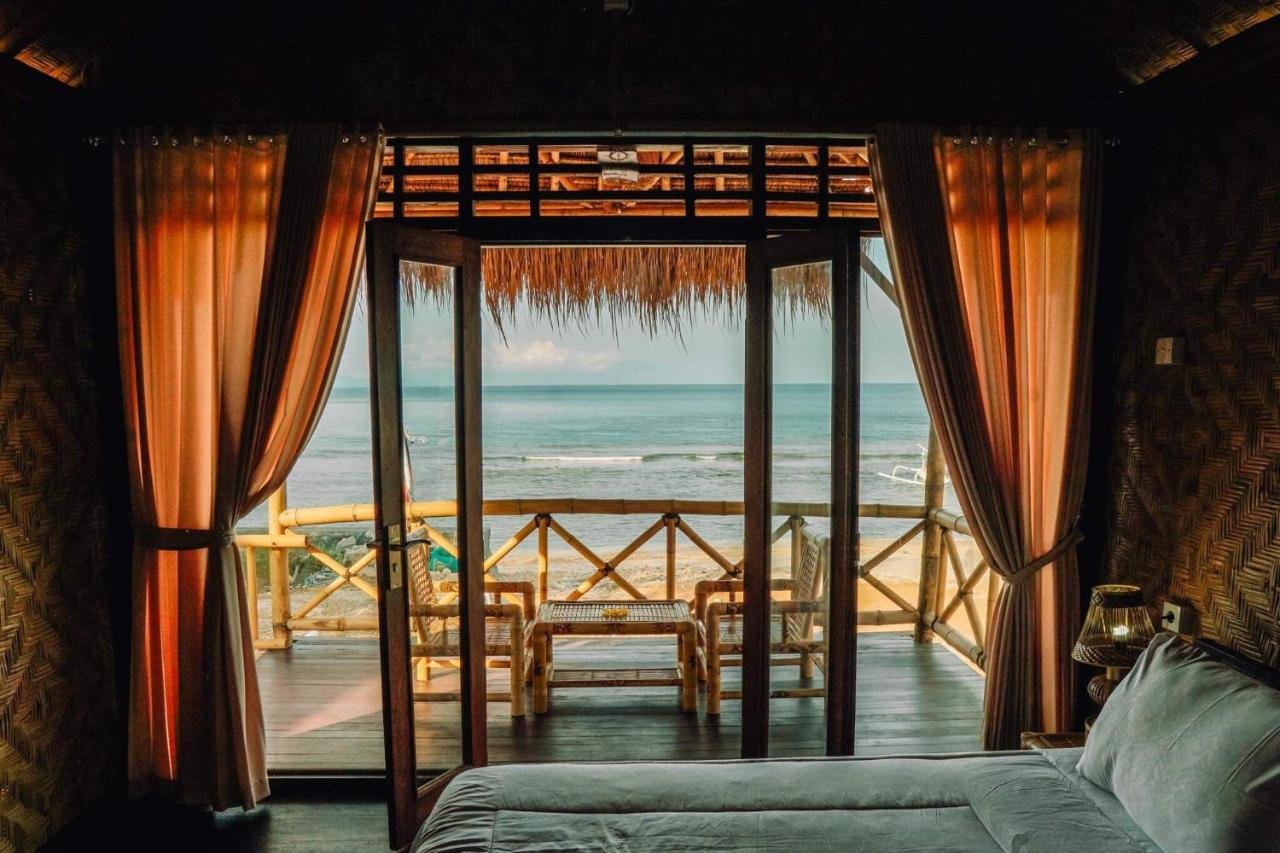 Beachfront bungalow with open sliding doors, bamboo furniture, and ocean view