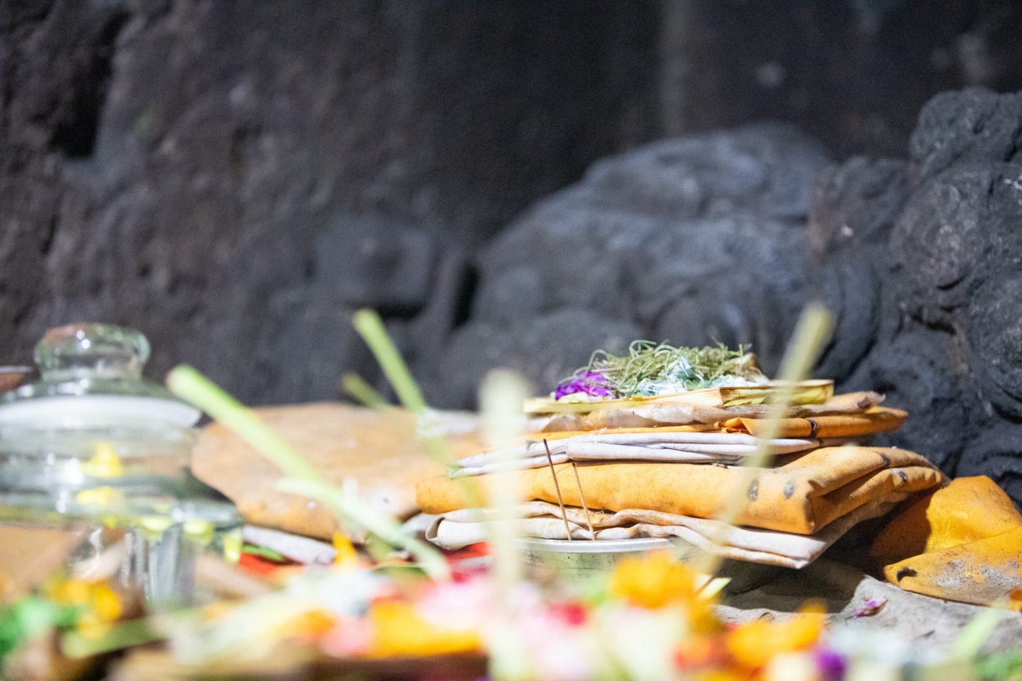 Stack of folded cloth and offerings with flowers on top, placed on a stone surface inside a dimly lit setting.
