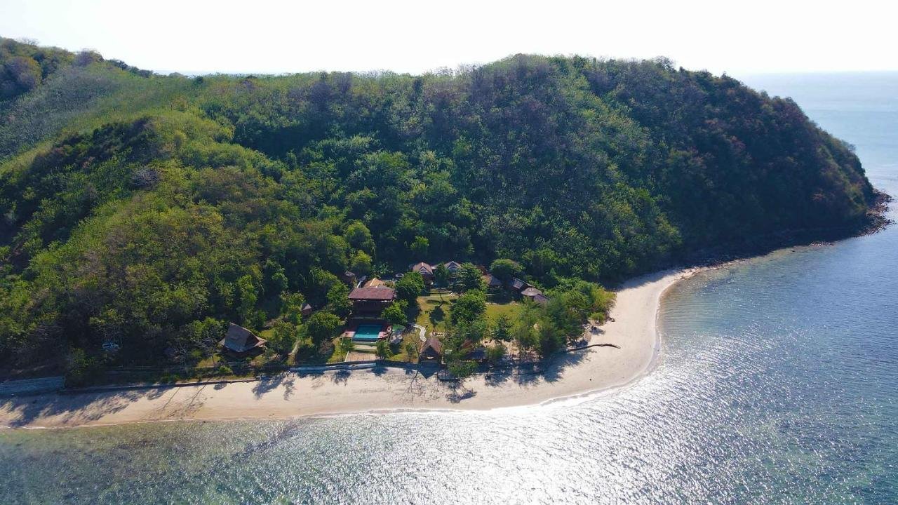 Aerial view of a tropical beach with lush green hills and a cluster of cottages near the shoreline.
