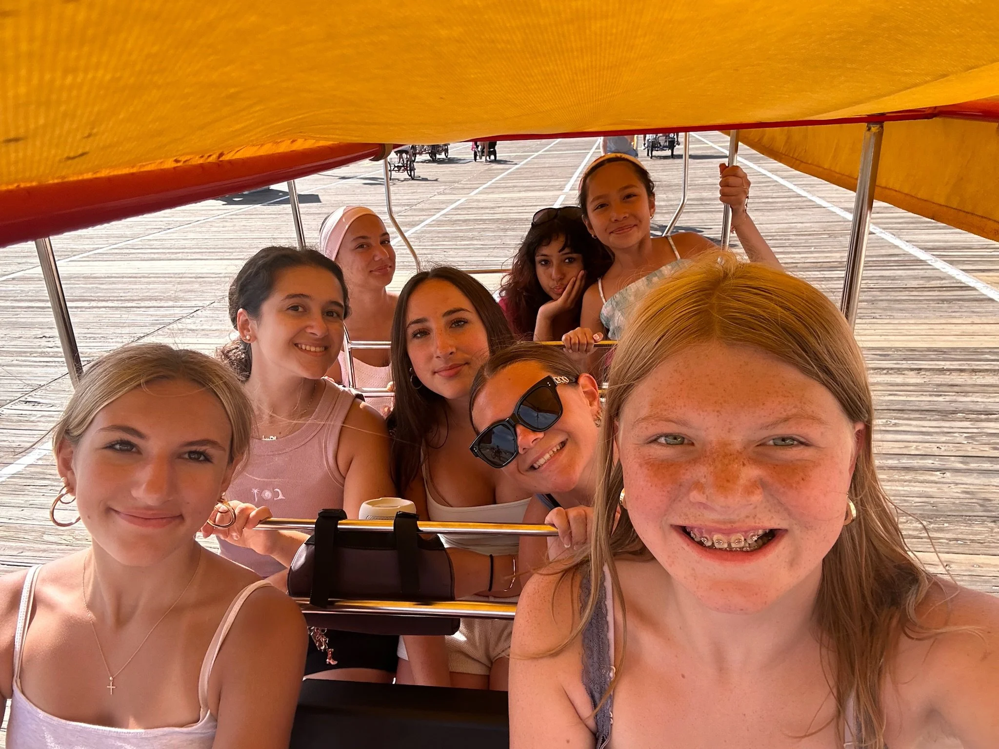 A group of young women and girls taking a selfie inside a yellow and red boat on a wooden dock.