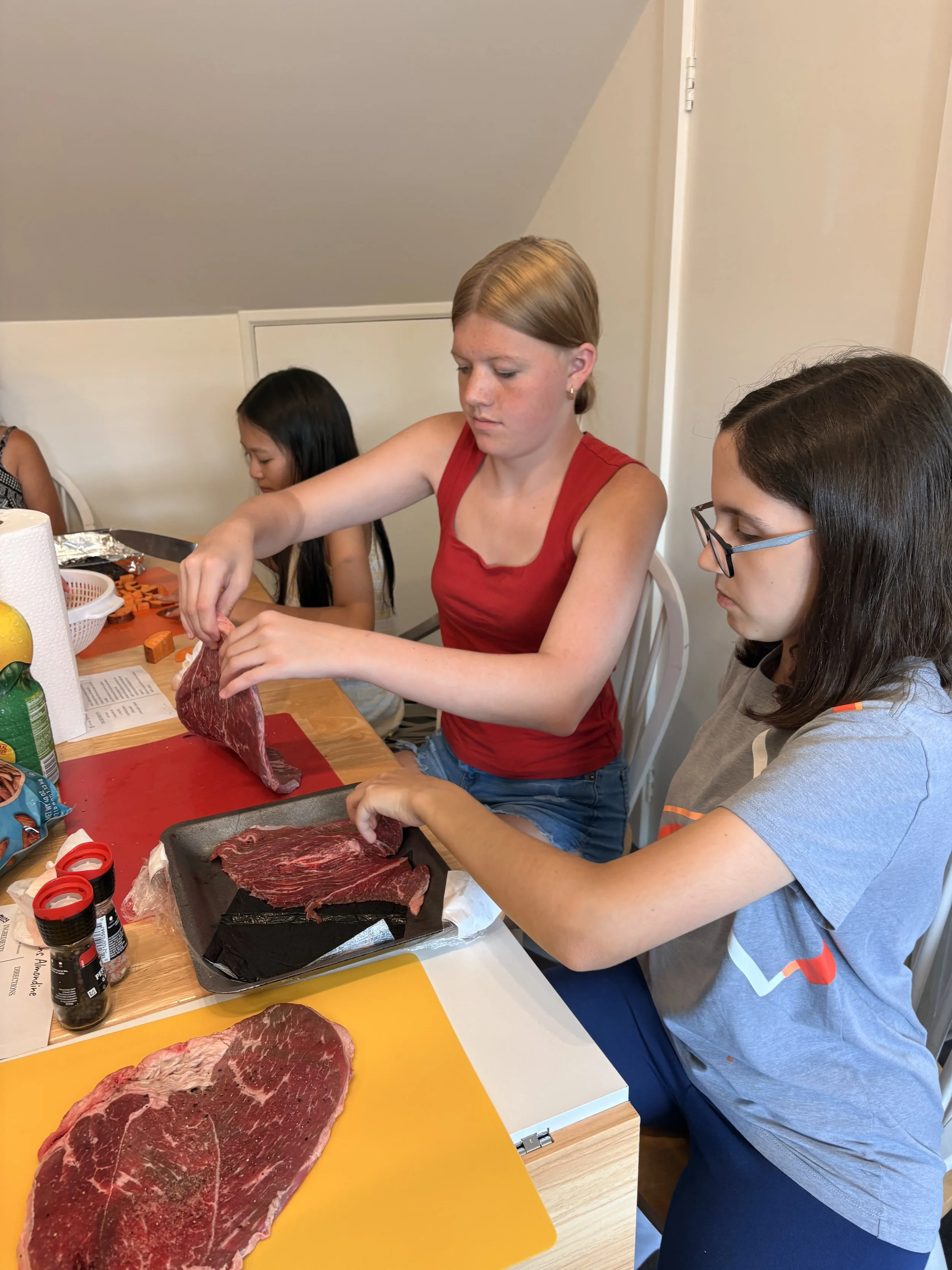 People preparing slices of raw beef in a kitchen.