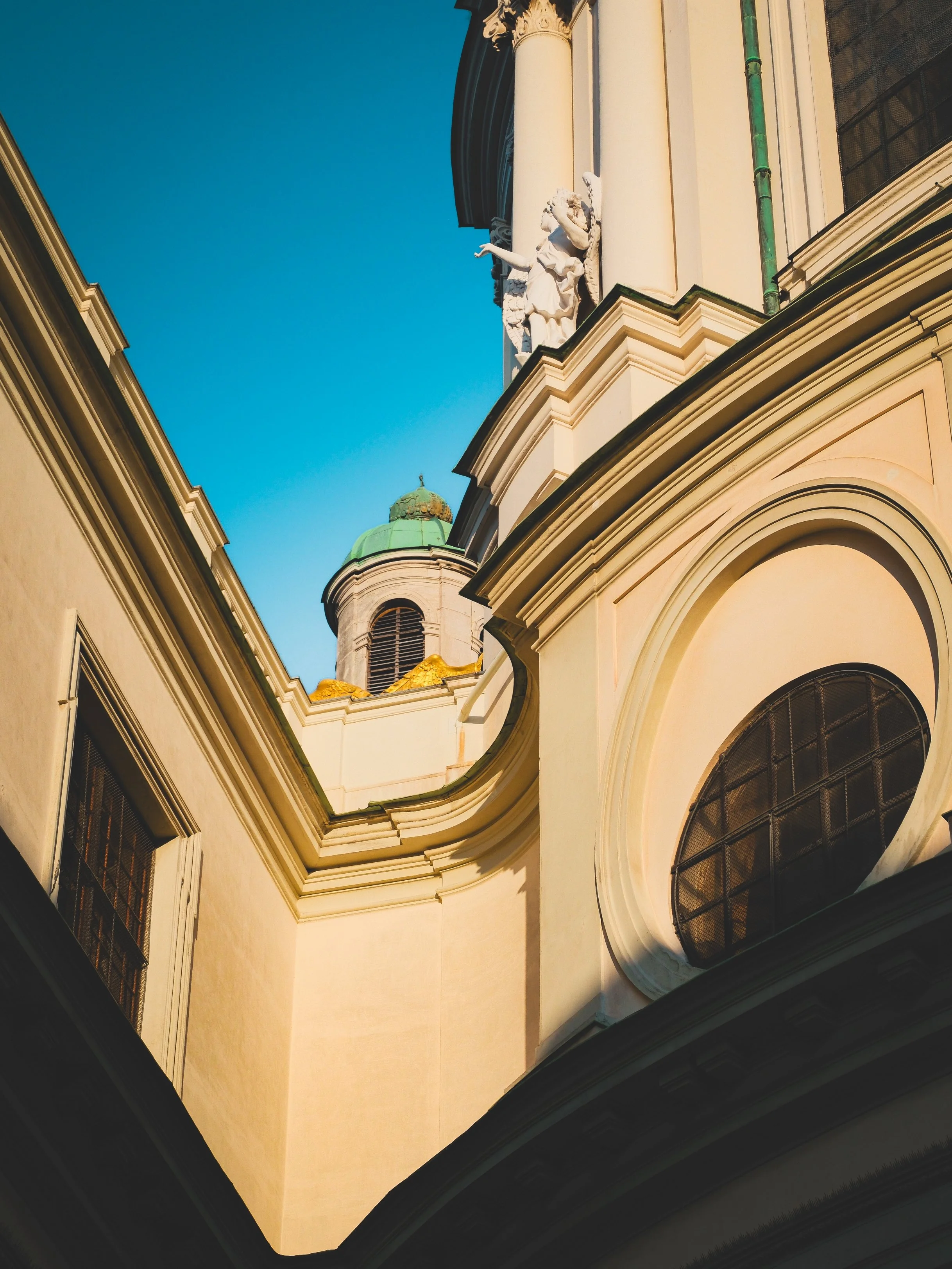 Photos of a historic European church or cathedral with detailed architectural features, statues, and a green-domed tower against a blue sky.