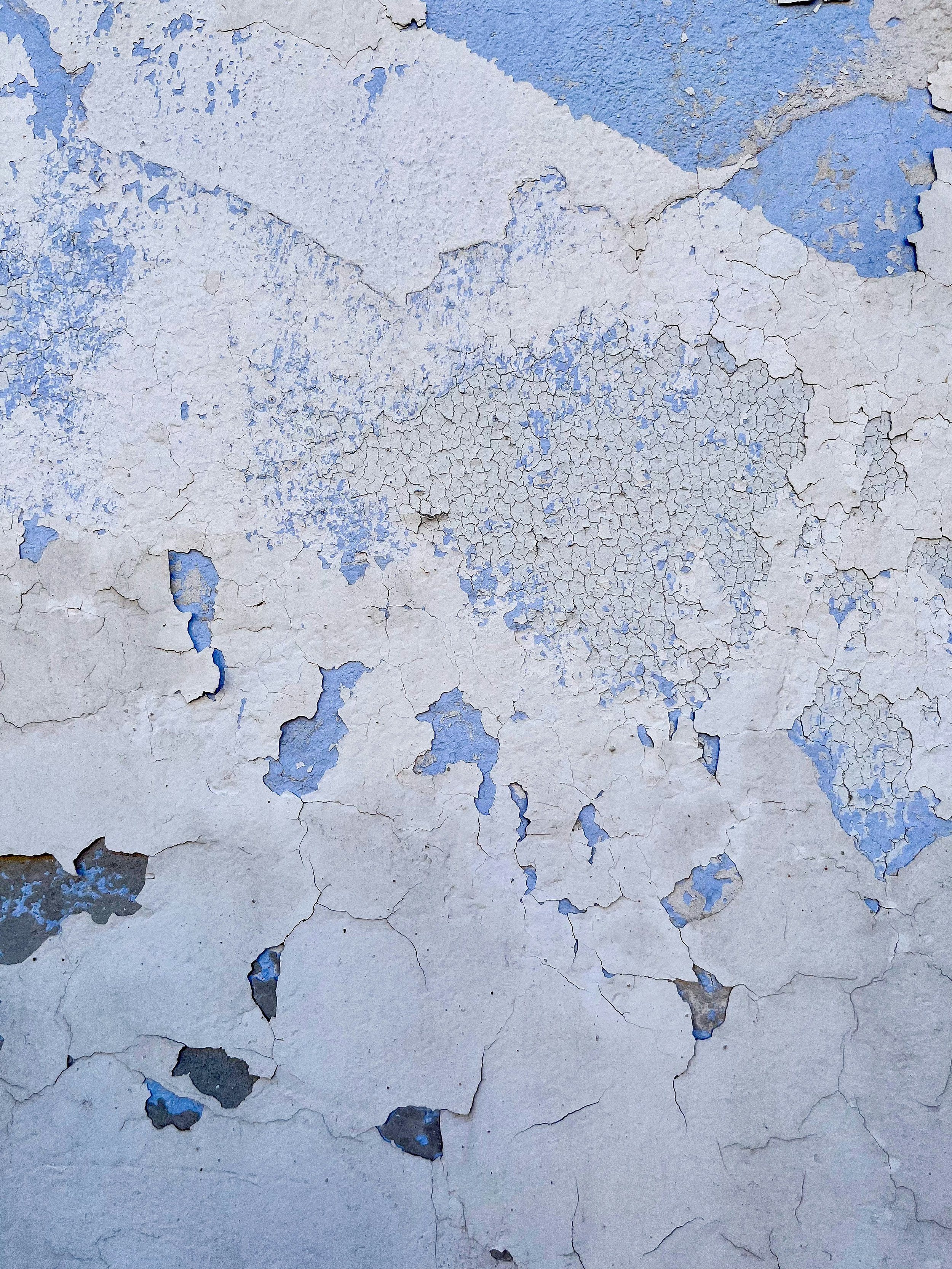 Close-up of a wall with peeling paint revealing multiple layers of white and blue paint underneath.