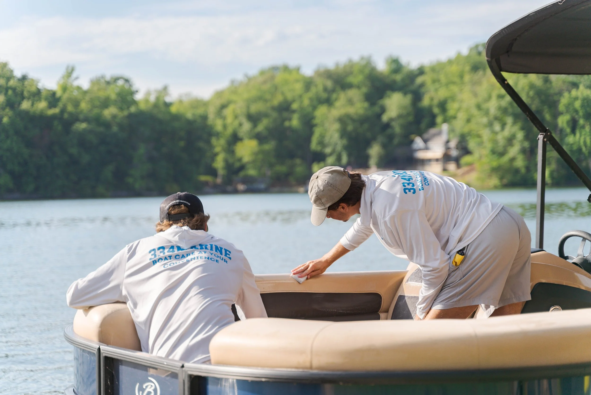Two people cleaning a boat on a lake with trees and houses in the background.