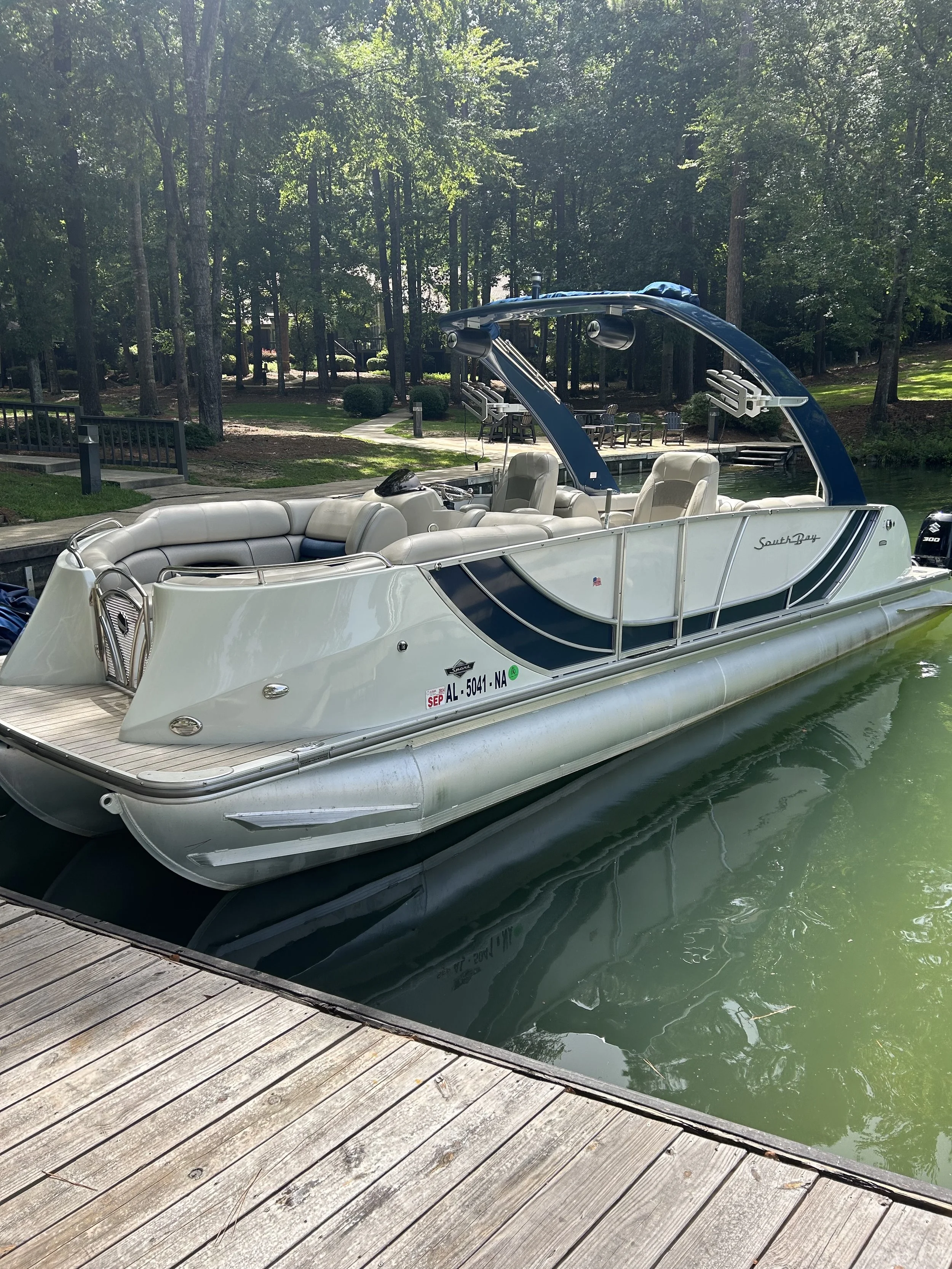 Luxury pontoon boat docked at a wooden pier on a lake surrounded by trees.