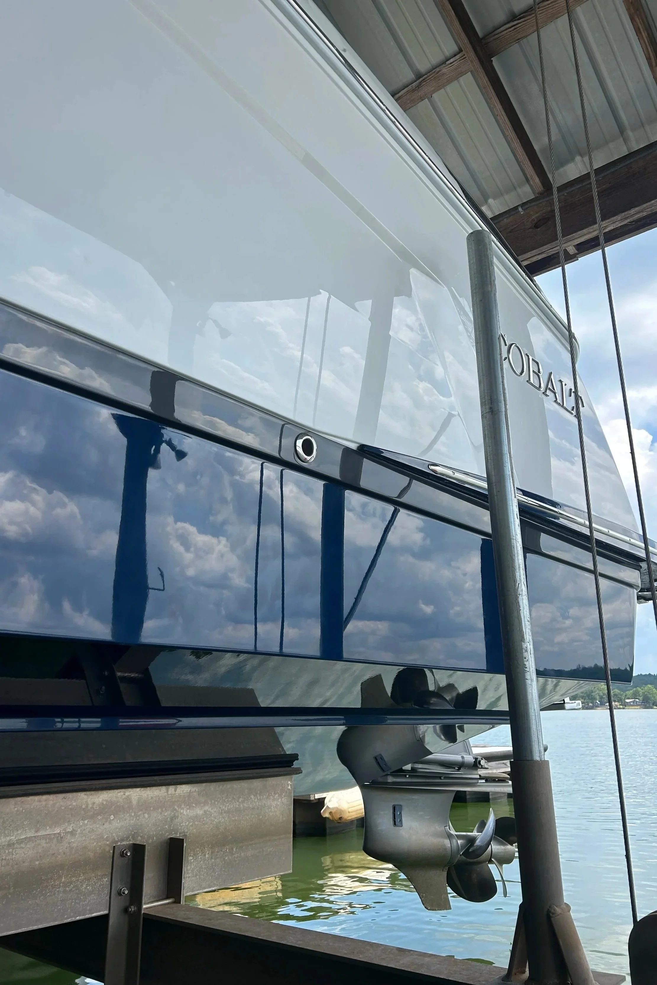Three bottles of yacht surface polishing products placed on a wooden surface outdoors, with a boat and a wooden post in the background.