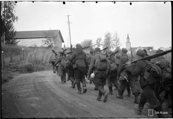 A group of soldiers walking along a dirt road carrying rifles during wartime in a rural area.