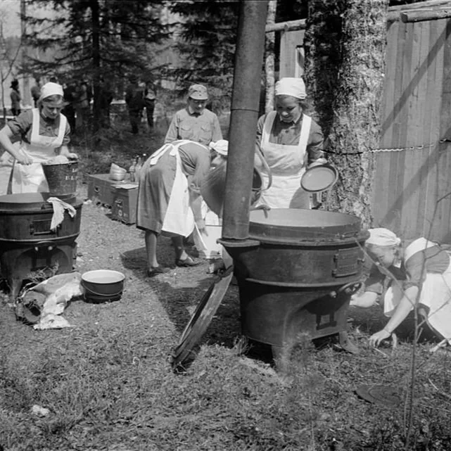 The Lotta Svard tending to outdoor stove  in a wooded outdoor setting during WW2.
