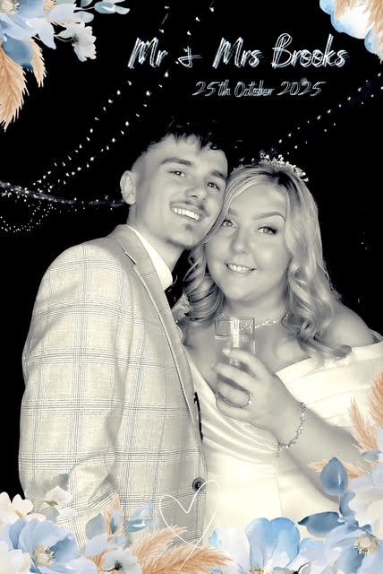 A black and white photo of a couple at a wedding, with the text 'Mr. & Mrs. Brooks 25th October 2025', framed by floral decorations. The couple is smiling, with the woman holding a drink.