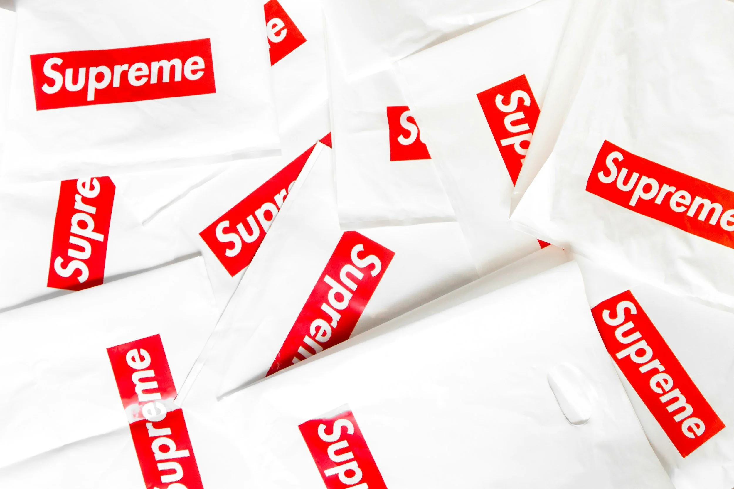Multiple plastic bags with red and white Supreme logos, crumpled on a white surface.