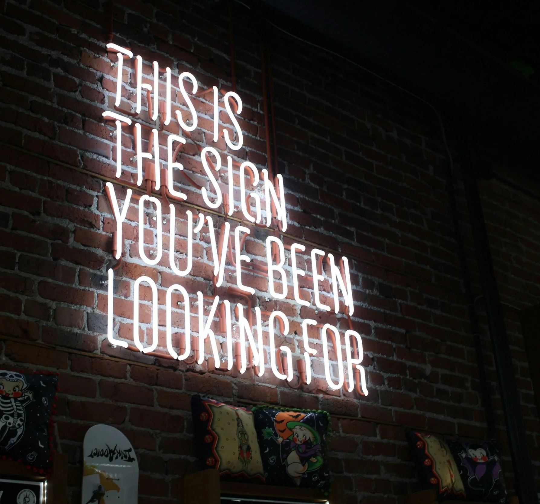 Neon sign on brick wall with the text: "This is the sign you've been looking for" in uppercase white letters.