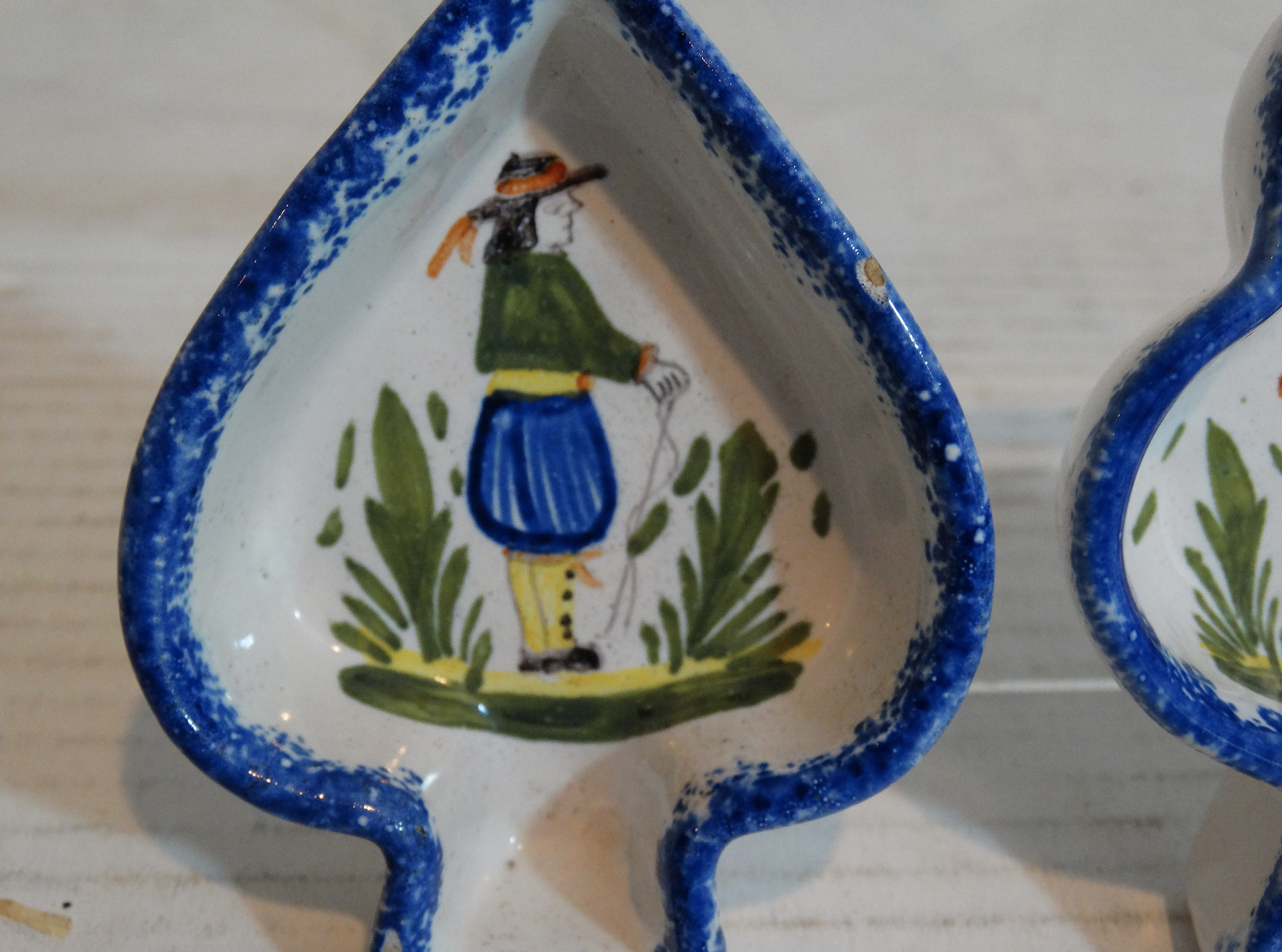 Set of two charming French faience Quimper butter pats in spade and club shapes with painted traditional Breton man and woman figures. Located in Austin, Texas.