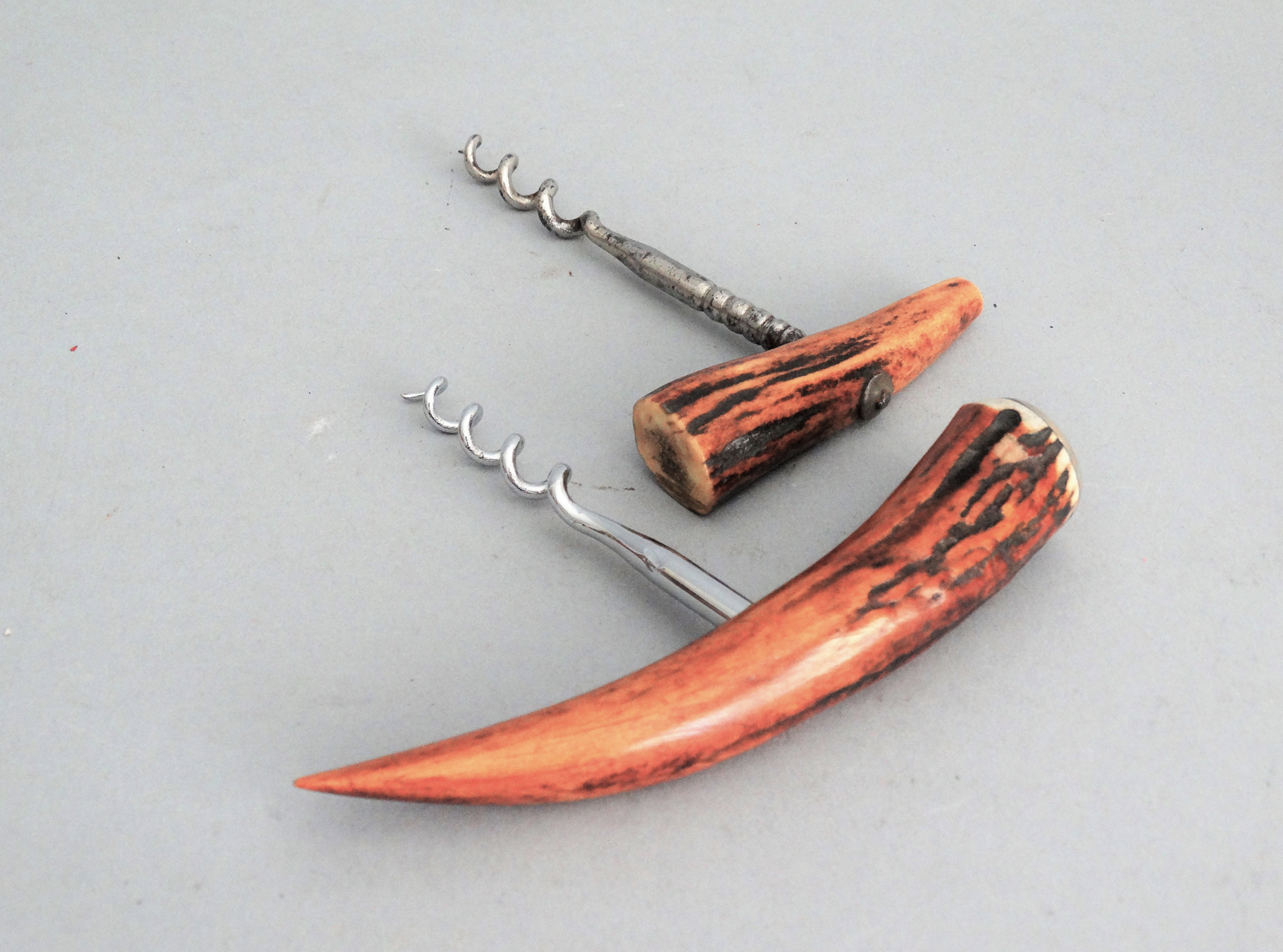 An early to mid 20th-Century continental set of two natural antler corkscrew bottle openers. The are bone antler with a metal screw. They are functional and decorative. Located in Austin, Texas.