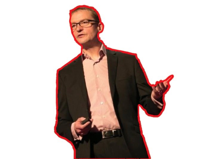 A man in a black suit, pink shirt, and glasses giving a presentation, outlined in red.