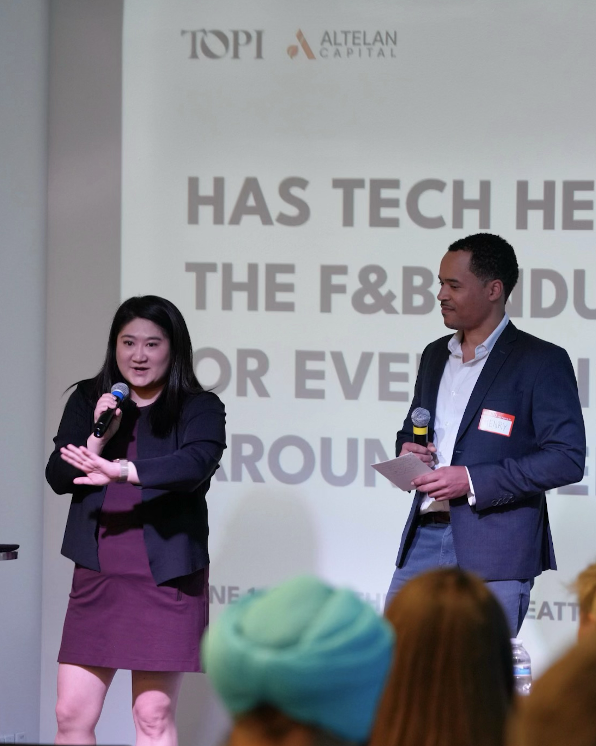 Two people on stage, Joann Jen speaking at a Topi Topics event. Has Tech Helped the Food and Beverage Industry?