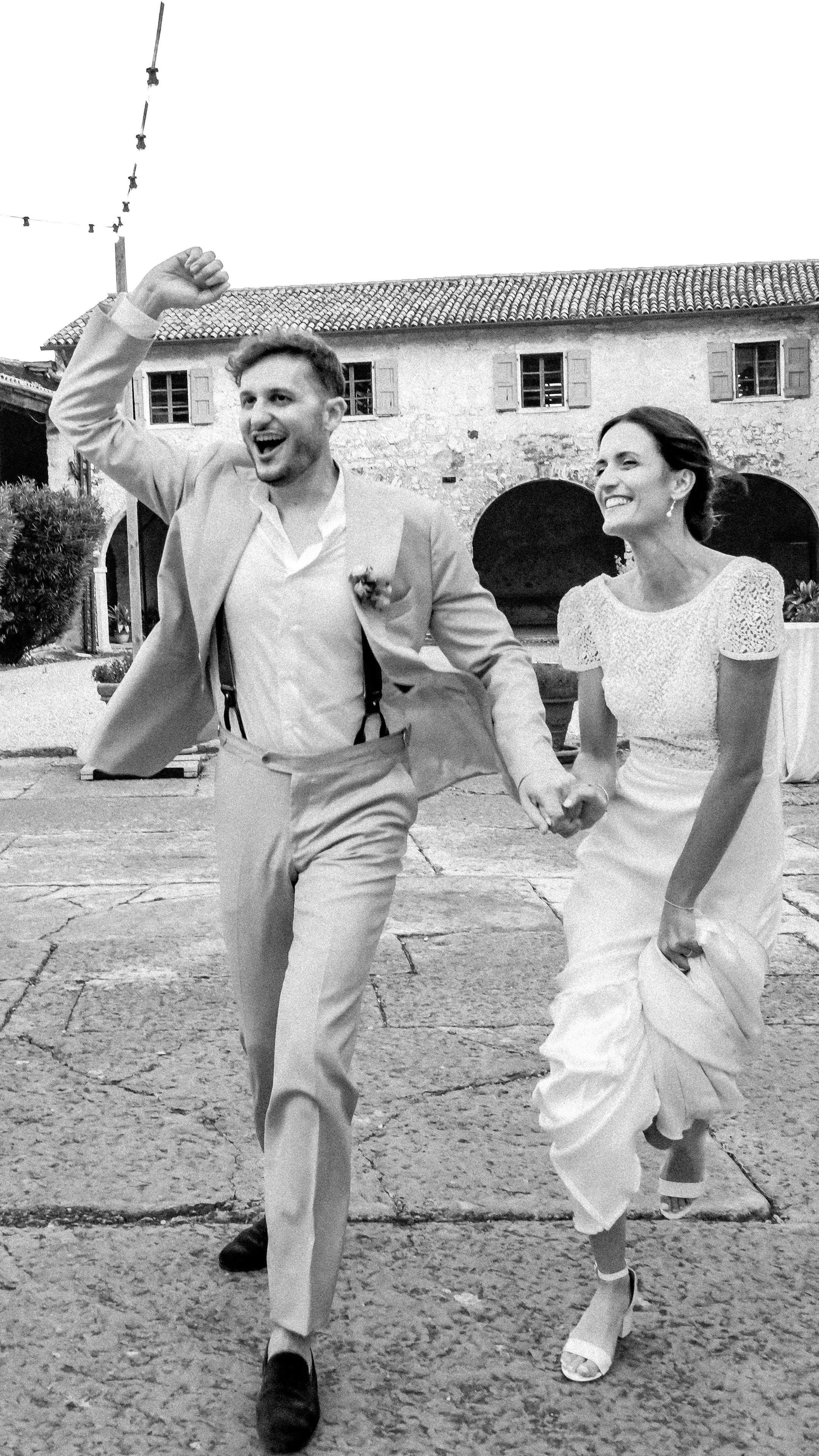 Nela and Davide laughing and running hand in hand across the stone courtyard of Serego Alighieri after their wedding ceremony near Verona.