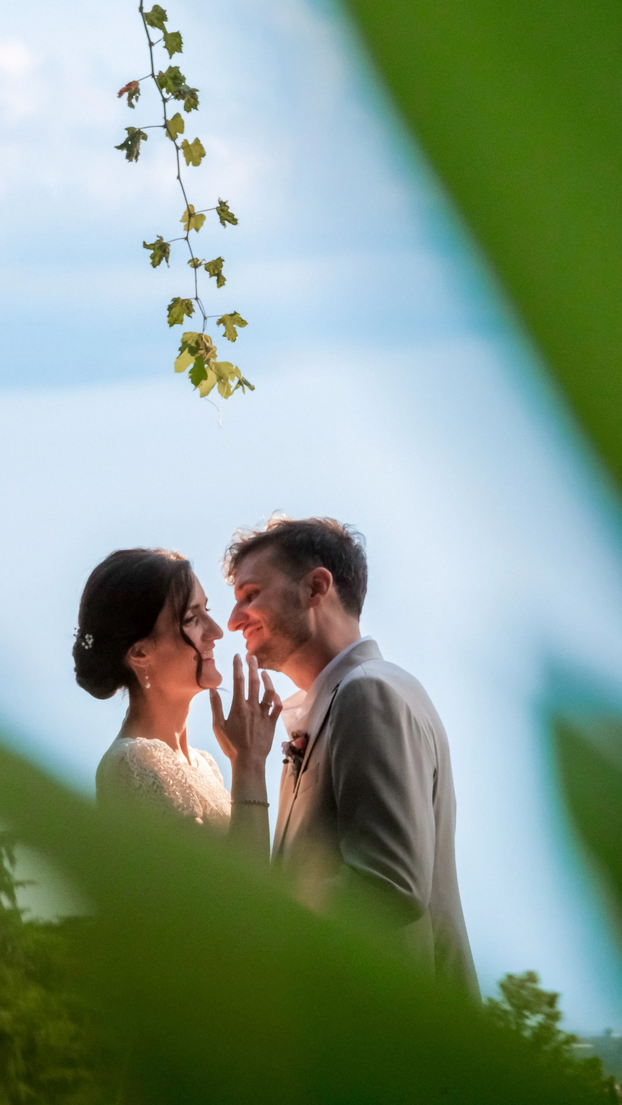 Bride and groom sharing an intimate moment, smiling face to face and framed by green leaves at their Serego Alighieri wedding near Verona.