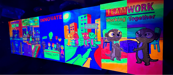 Four people standing in front of a colorful 'Happy Birthday' banner with neon decorations. They are holding drawings and standing in a decorated room with neon art and string lights.