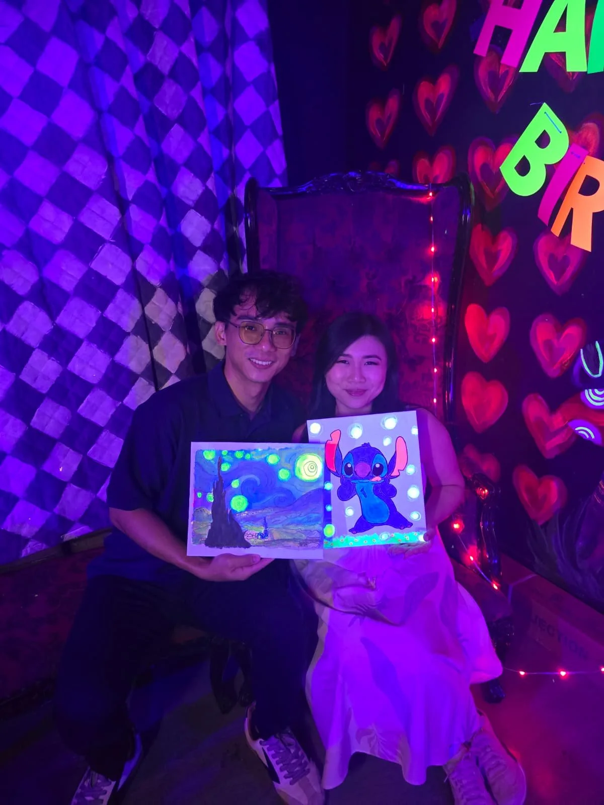 Girl with a glowing headband creating a neon-colored painting of a cartoon character on paper at a glow-in-the-dark art event.