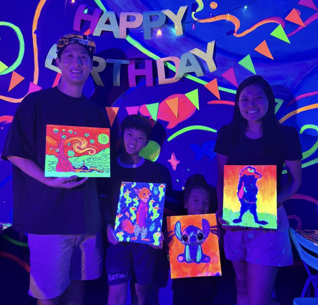 Family celebrating a child's 5th birthday with a cake, colorful decorations, and a 'Happy Birthday' banner in the background.