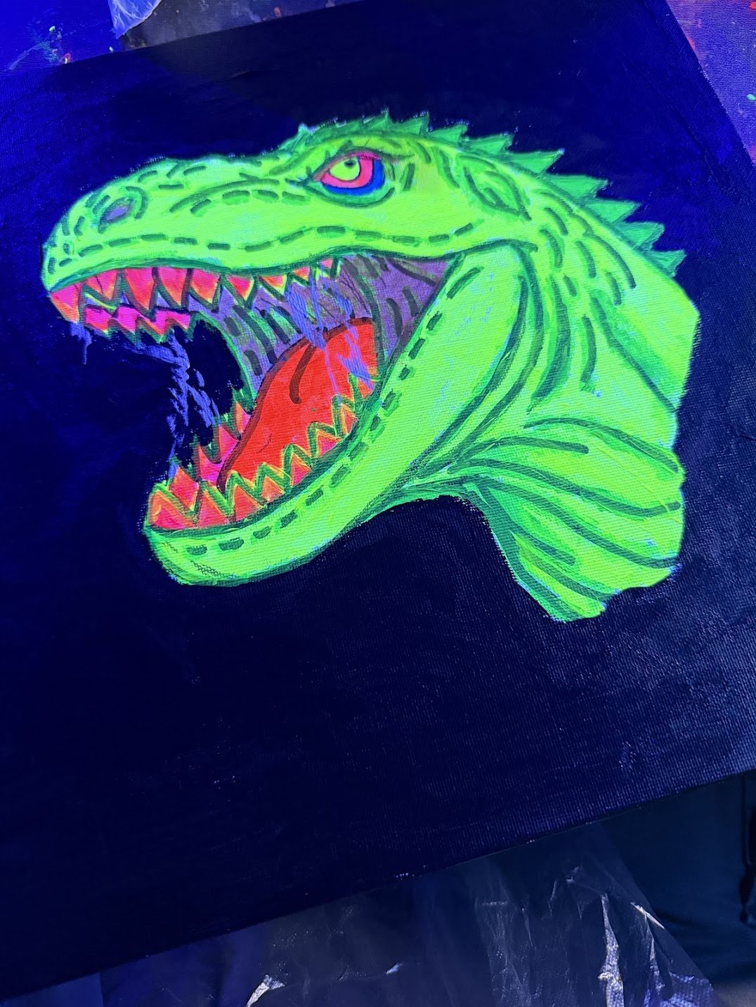 Neon-colored drawing of a T-Rex with its mouth wide open, showing sharp teeth and a red tongue, on black fabric.