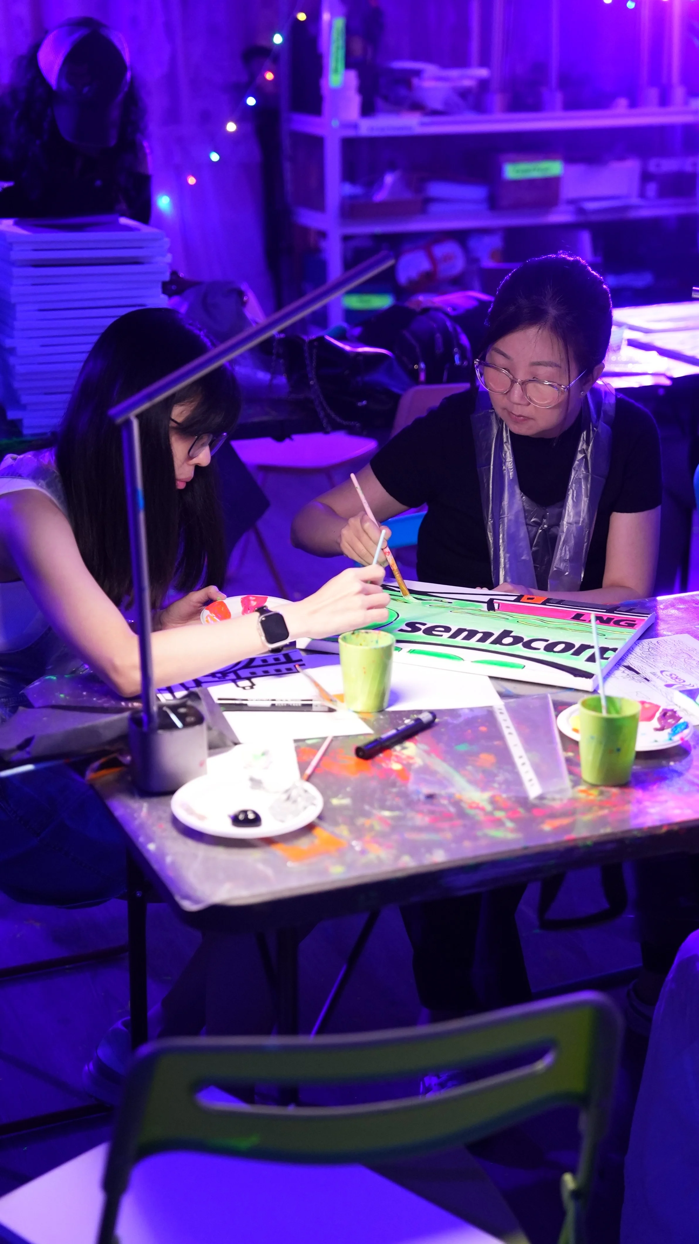 Girl with a glowing headband creating a neon-colored painting of a cartoon character on paper at a glow-in-the-dark art event.