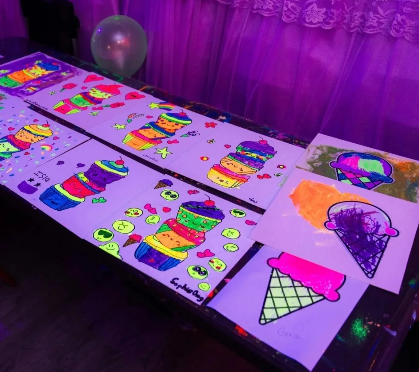 Girl with a glowing headband creating a neon-colored painting of a cartoon character on paper at a glow-in-the-dark art event.