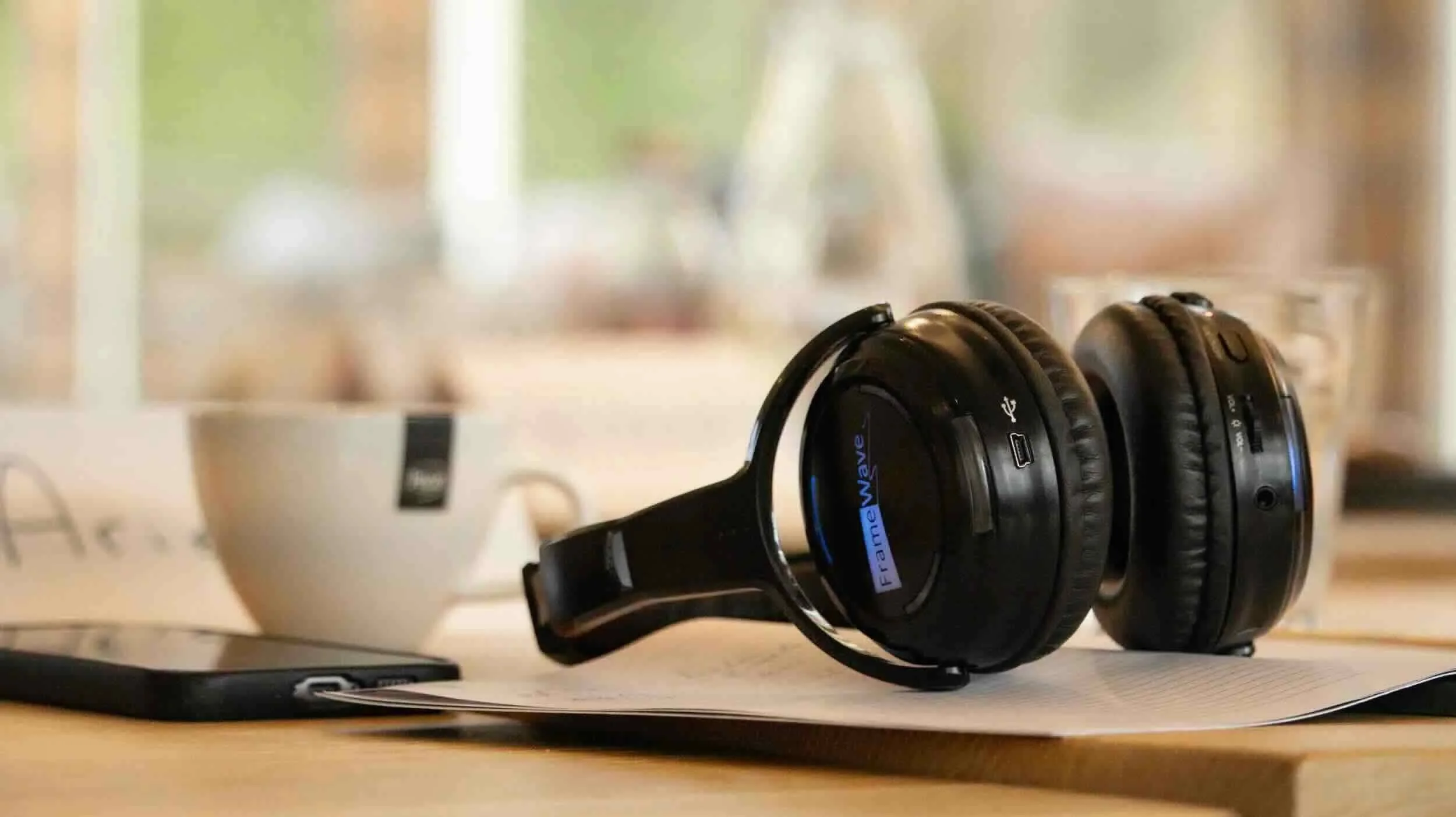 Draadloze koptelefoon, een kopje, een smartphone en een glas water liggen op een tafel. Dit is onderdeel van de lichaamstaal workshop.