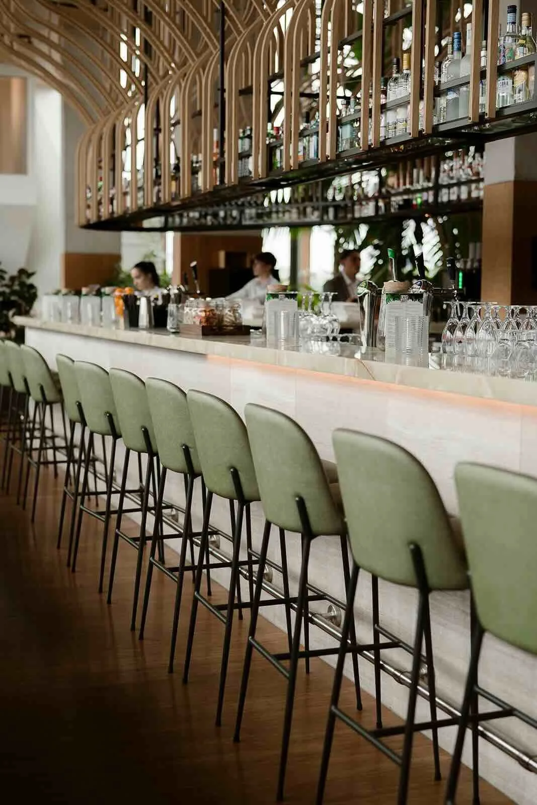 Training lichaamstaal en non-verbale communicatie. Interieur van een moderne bar- met een witte toog, groene barkrukken en een houten plafond met een decoratief houten element. Achter de bar zijn mensen die drankjes bereiden, en er zijn glazen en fle