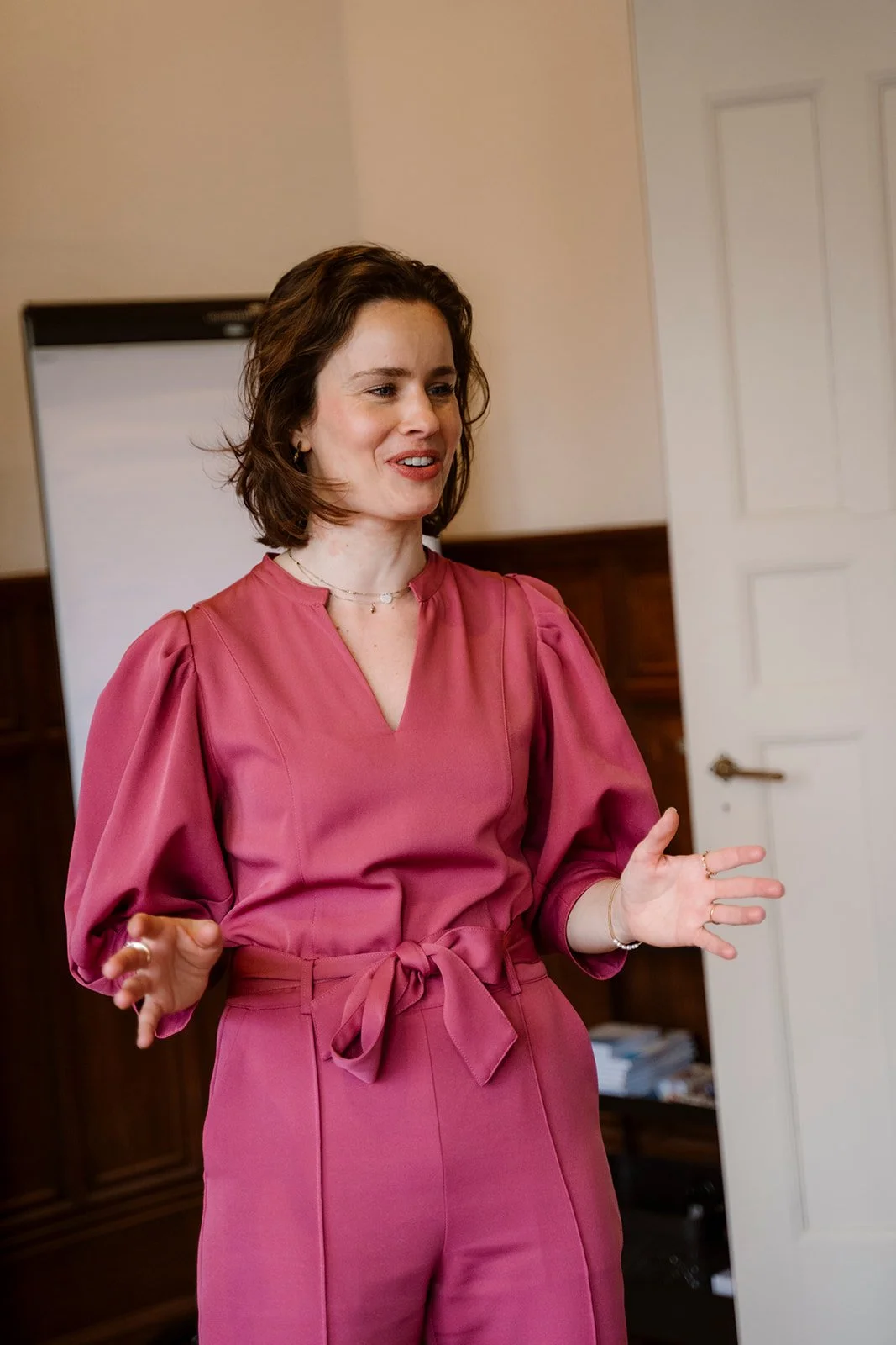 Vrouw, Lindy Bremer, geeft een training over Lichaamstaal in een roze jumpsuit in Den Haag.