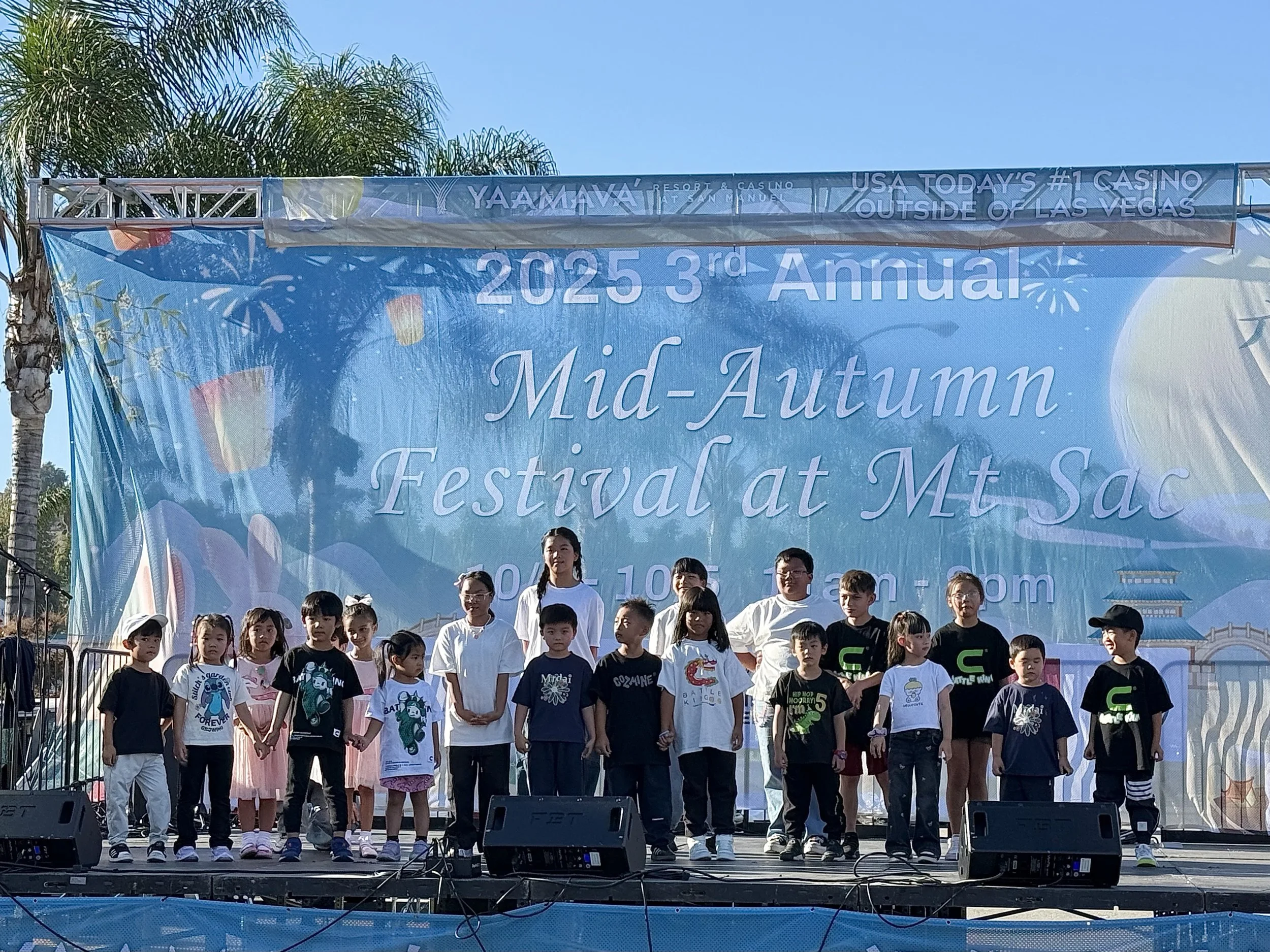 Children and adults standing on a stage with a large blue banner in the background that reads '2025 3rd Annual Mid-Autumn Festival at Mt. Sac'.