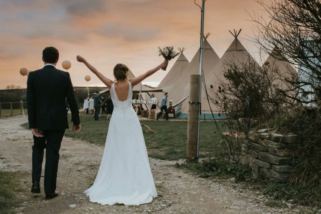 Couple celebrating outside wedding tipis at sunset