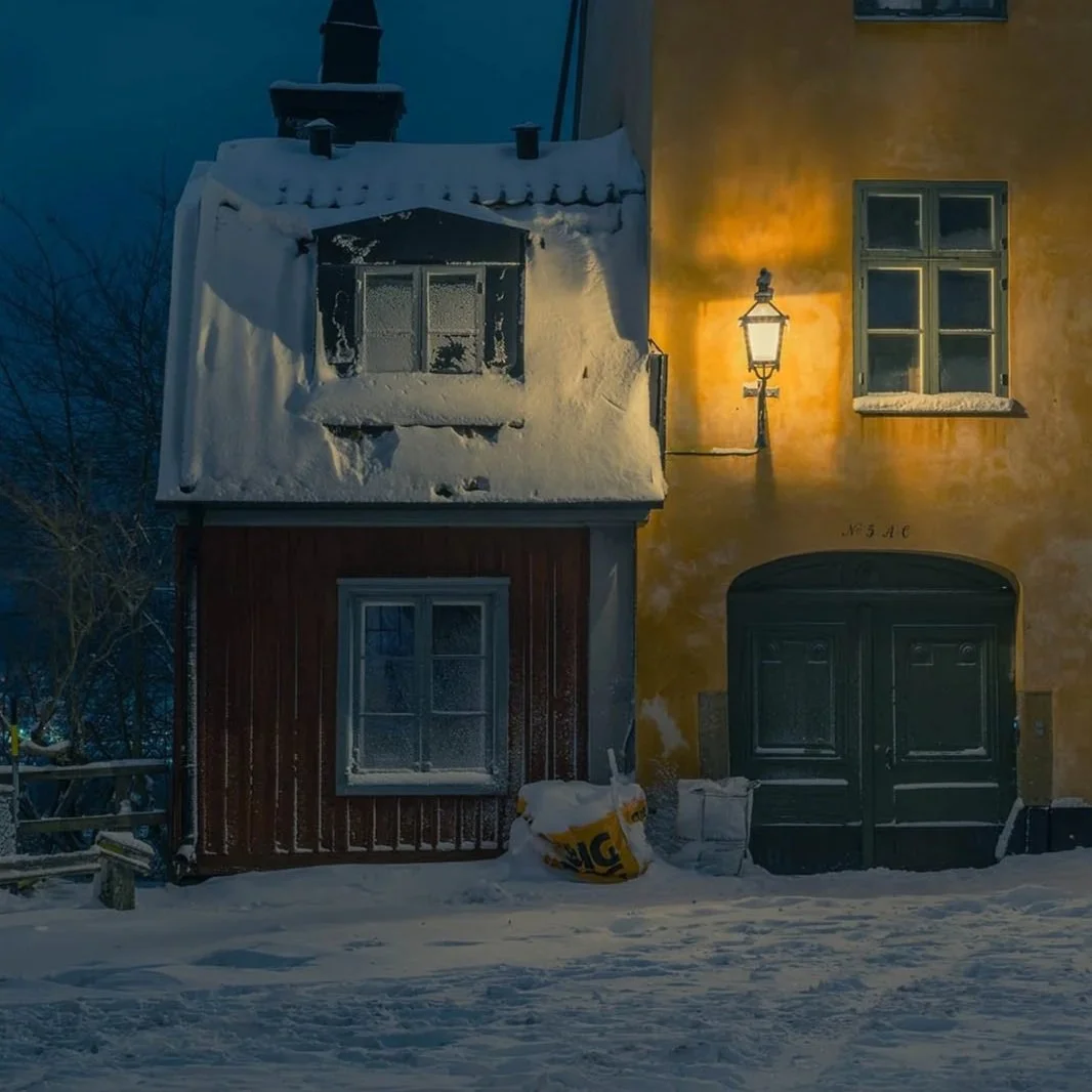 Snow-covered buildings illuminated by a warm streetlamp at night.