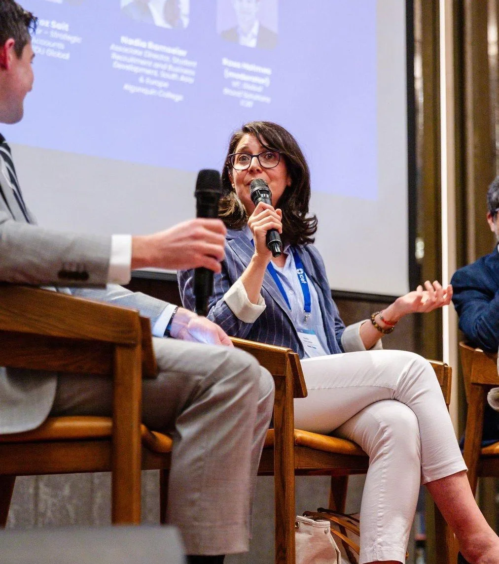 A woman with glasses speaking into a microphone during a panel discussion at an event.