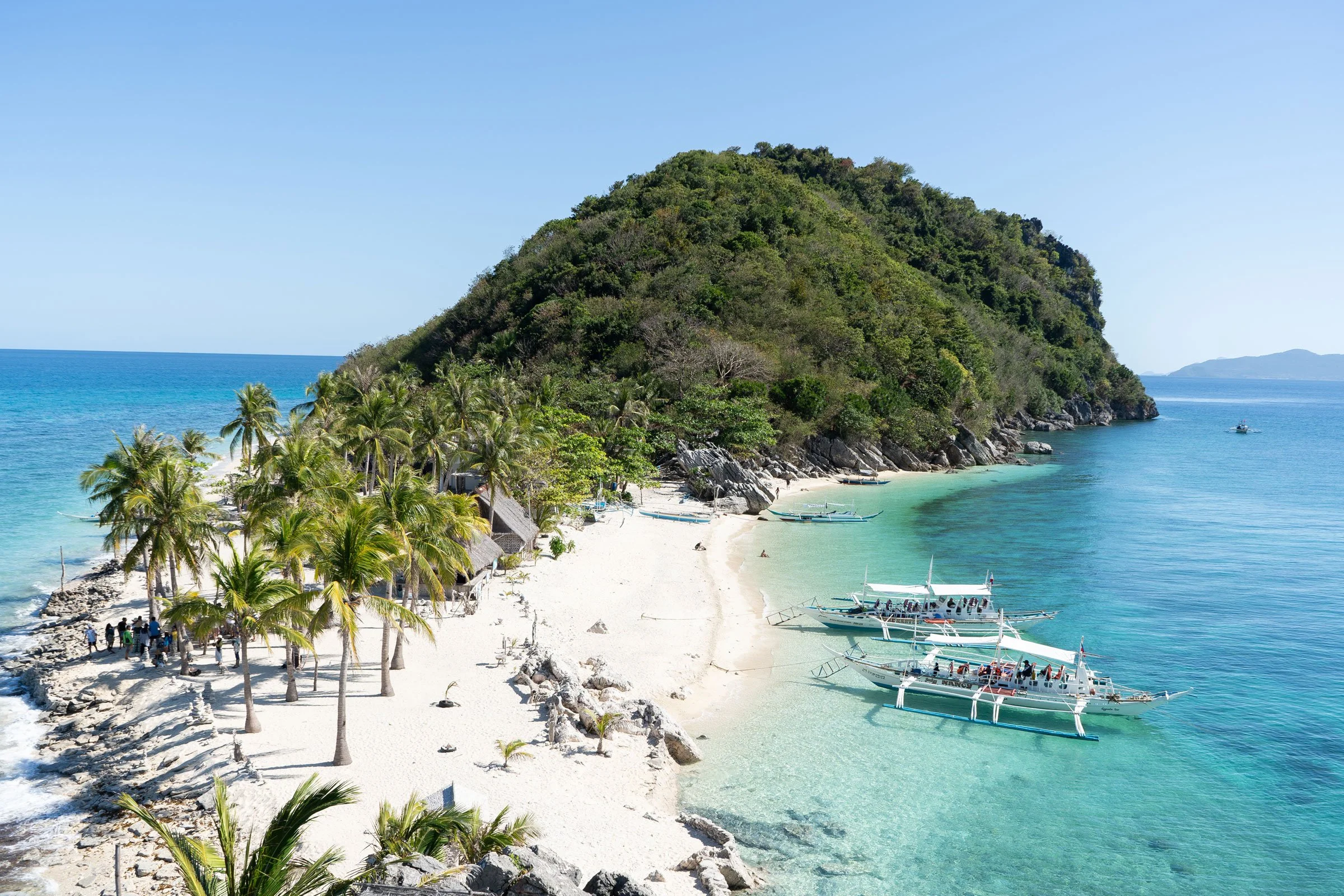Tropical island landscape in the Philippines with calm turquoise waters, lush green mountains, and traditional fishing structures—capturing the quiet beauty of slow island life.