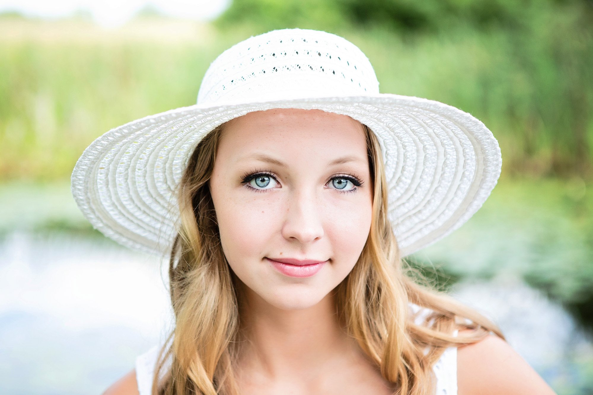 Young woman outdoors wearing a large white sunhat and smiling