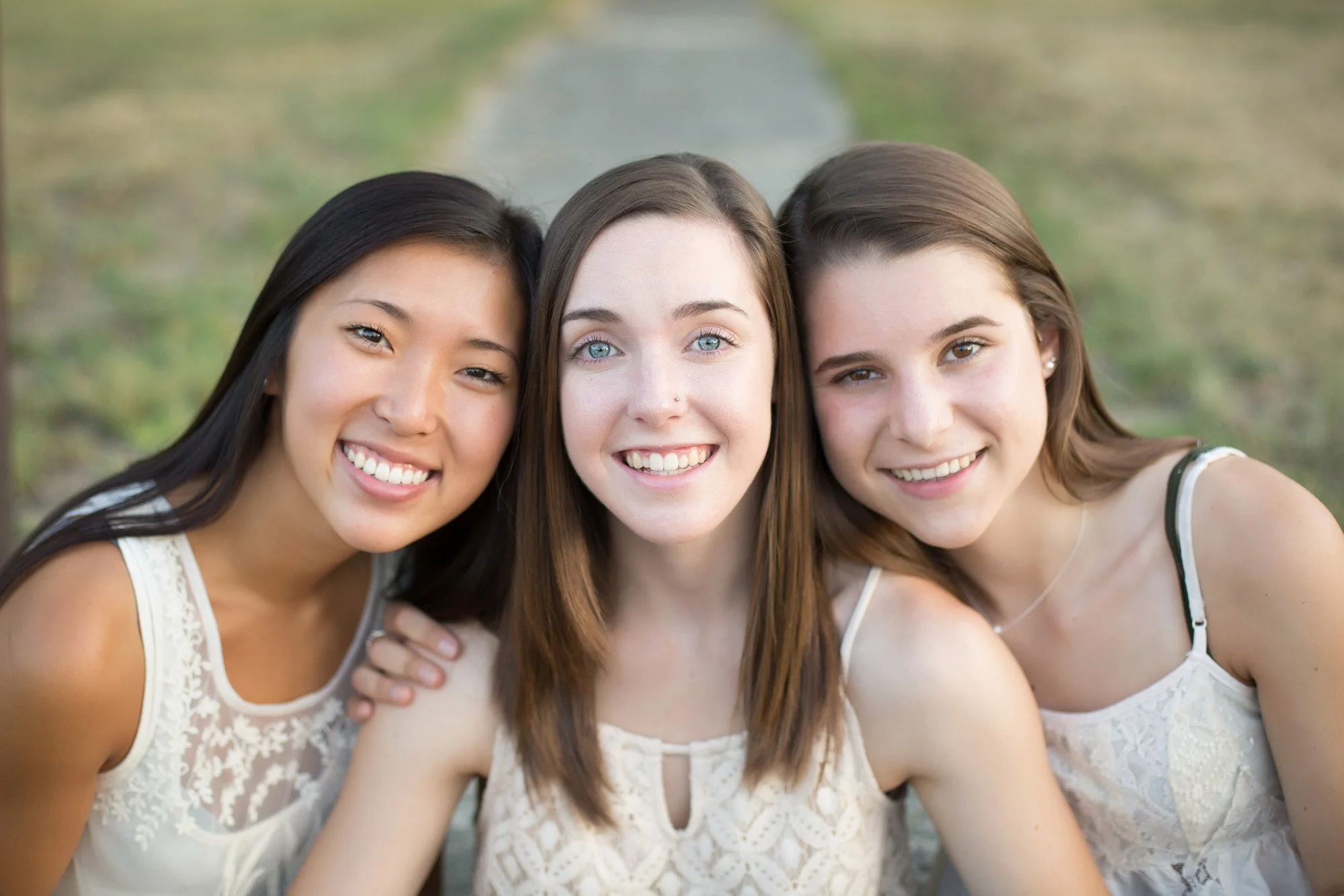 Three young women smiling close together outdoors.