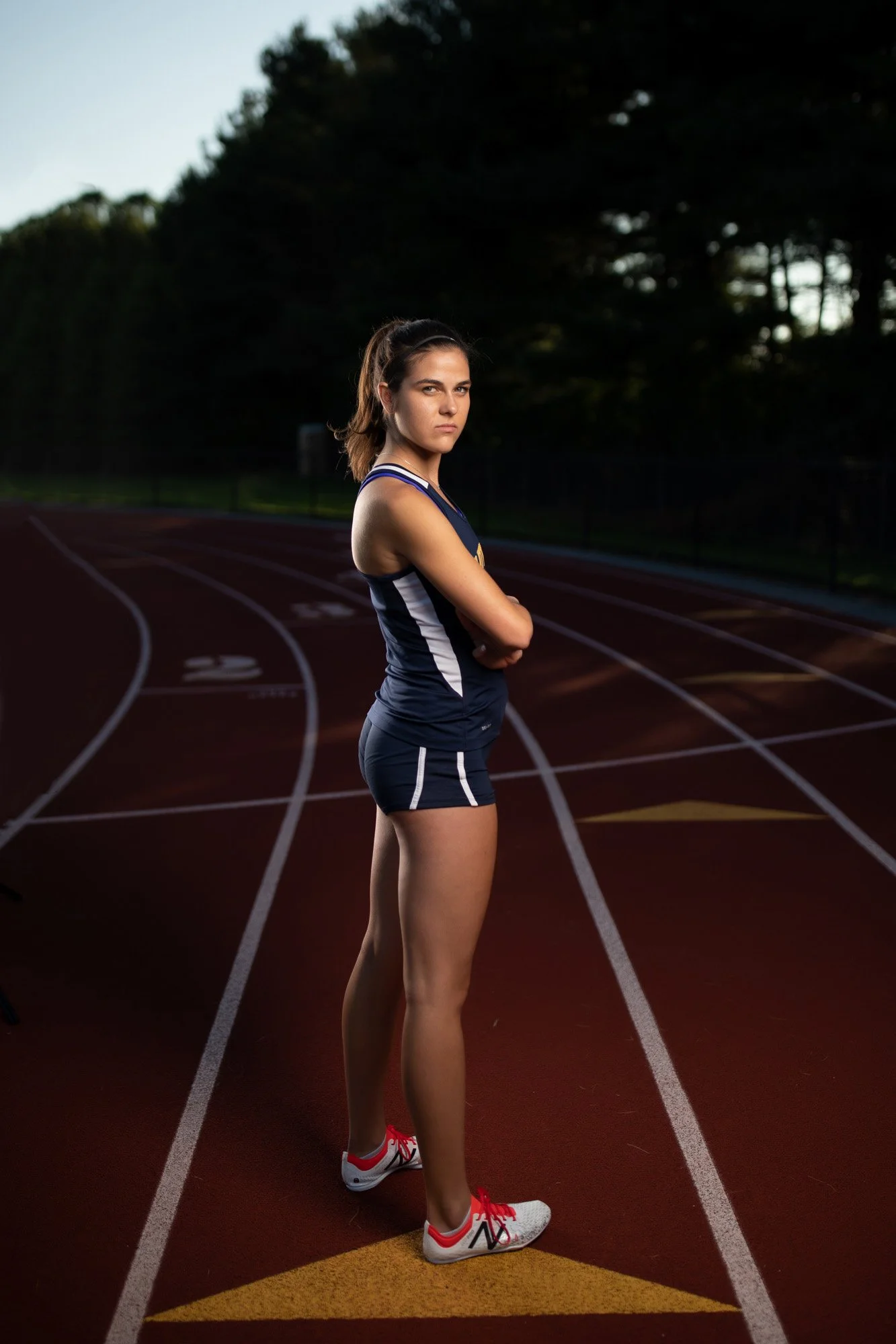 A young woman in athletic gear standing on a running track at dusk or dawn.