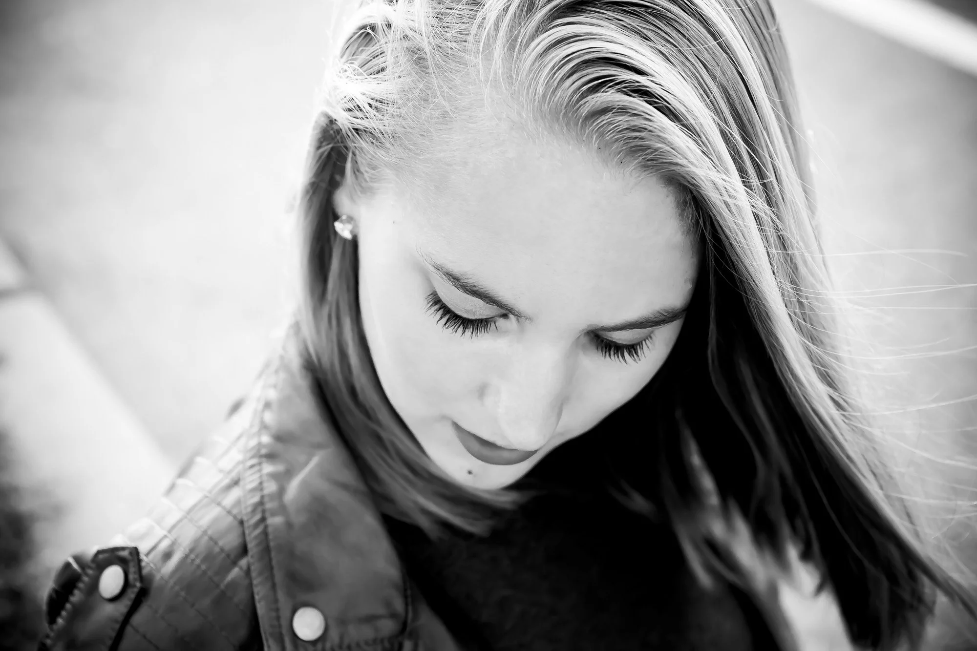 Black and white close-up of a young woman looking down with long hair, closed eyes, and an earring.