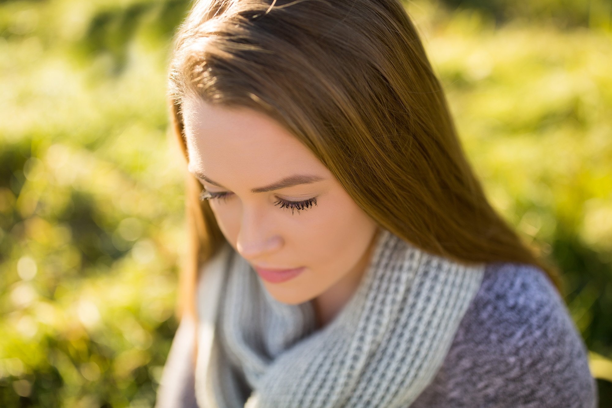 A young woman with long brown hair and closed eyes, outdoors, with a soft expression, surrounded by greenery.