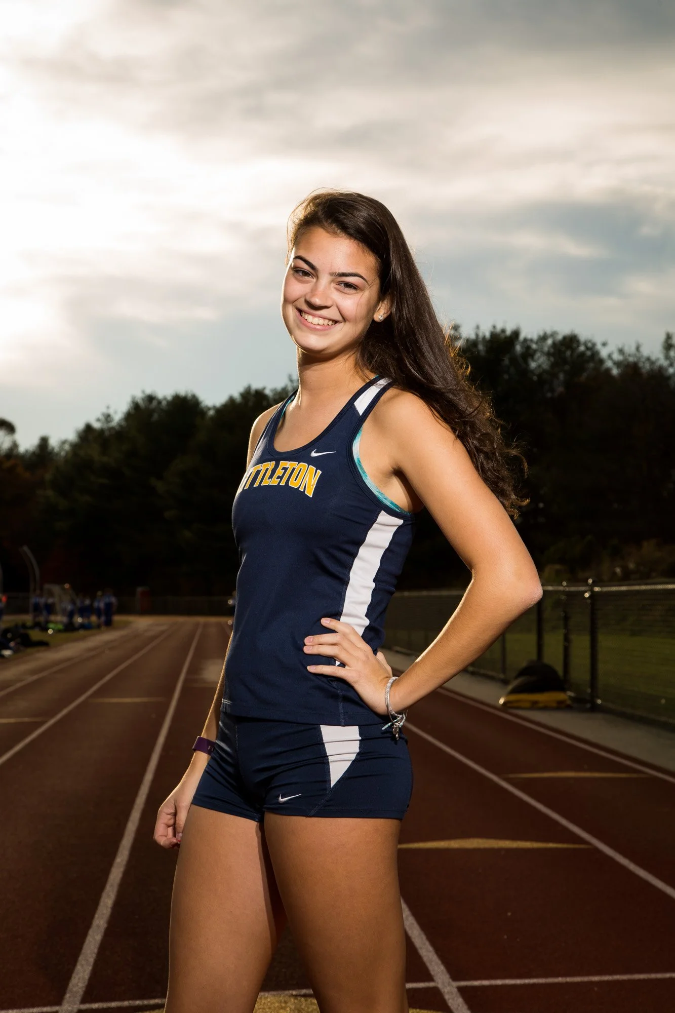 Young female athlete standing on a track field with a smile, wearing a navy blue sports uniform with white and yellow accents.