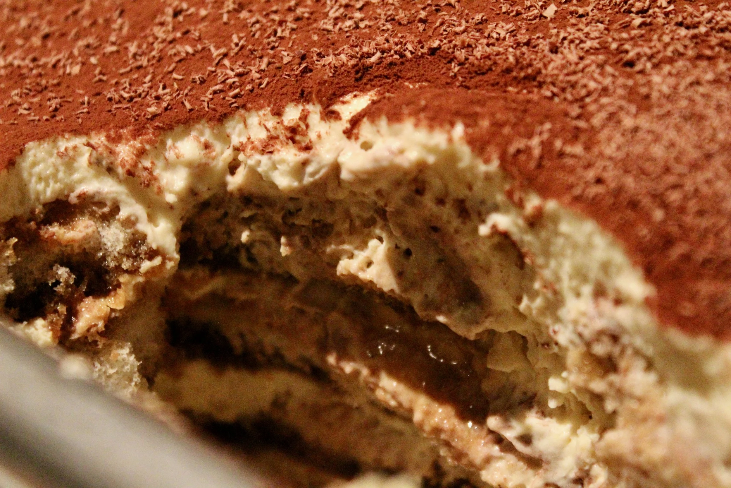 Close-up of a layered dessert with whipped cream, chocolate, and cocoa powder on top.