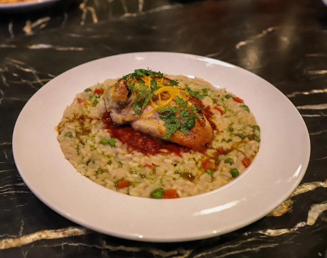 A plate of risotto with chicken and vegetables, garnished with herbs and lemon zest.