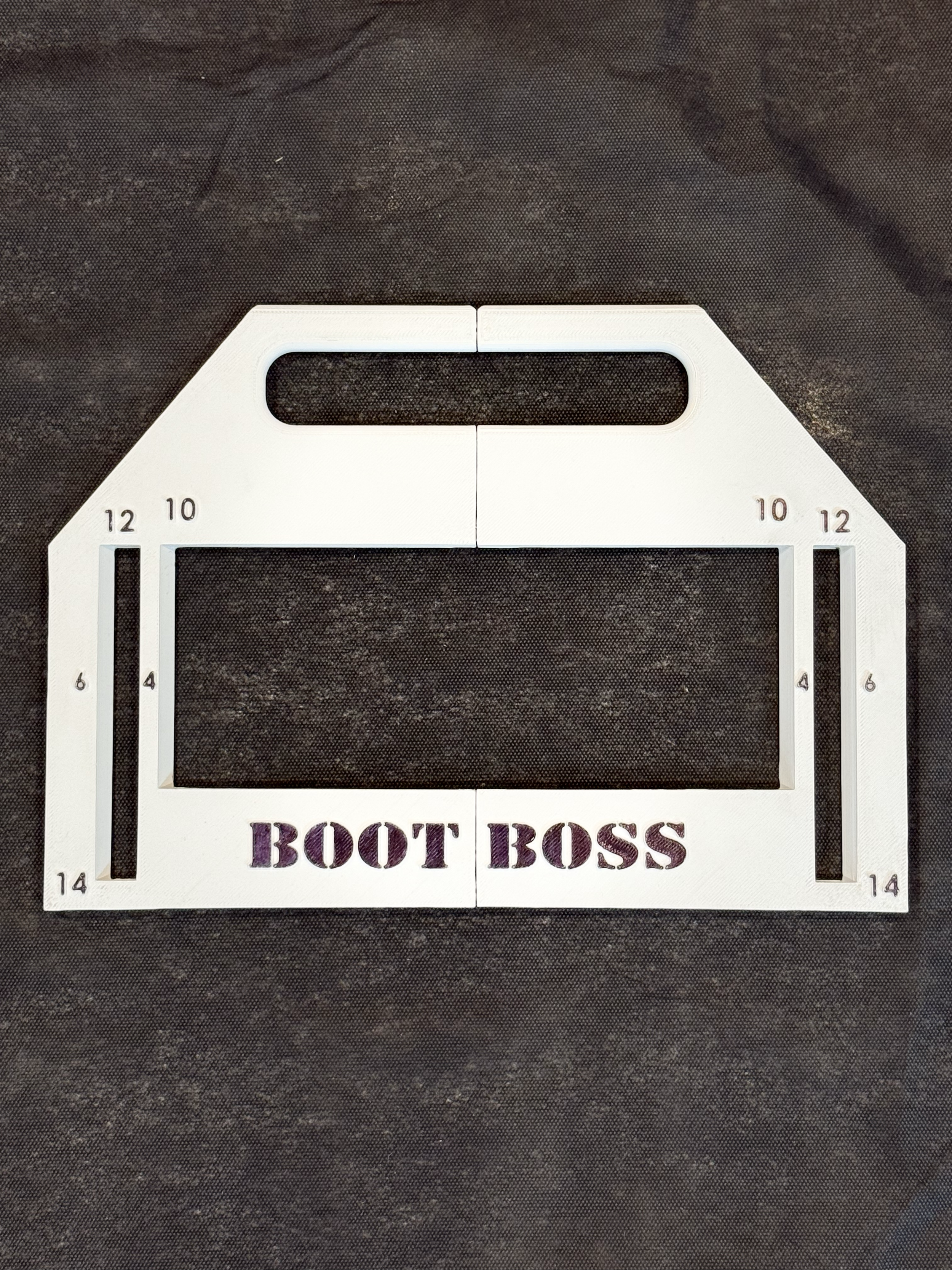 A white digital metering tape measure with the words 'BOOT BOSS' in purple below the rectangular screen, placed on a dark textured surface.