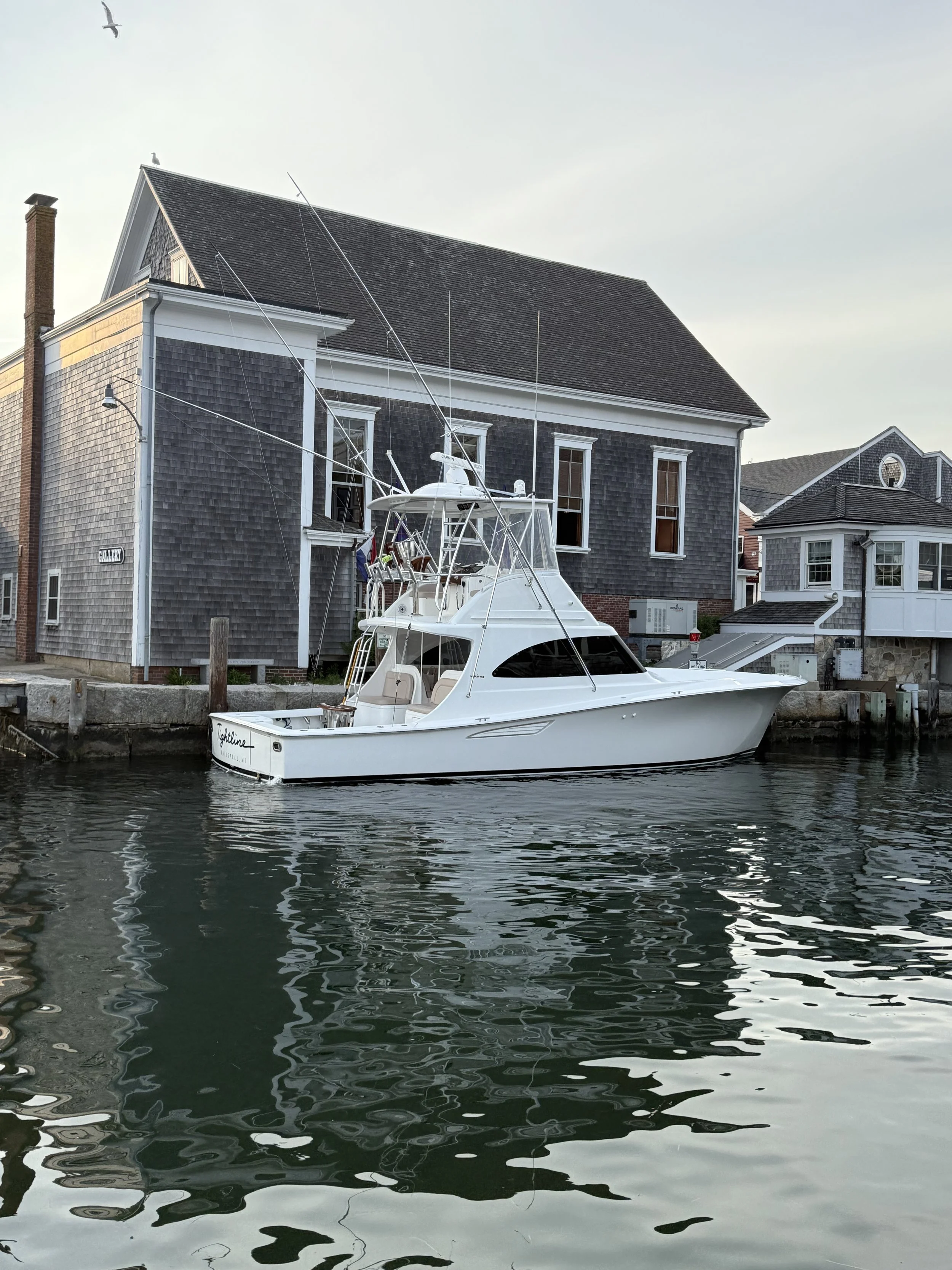 A white yacht docked at a harbor with houses in the background.